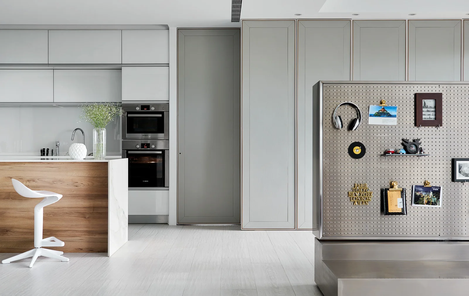 A modern kitchen featuring a wood-toned island, sleek grey cabinetry, and a metal pegboard room divider holding personal items.