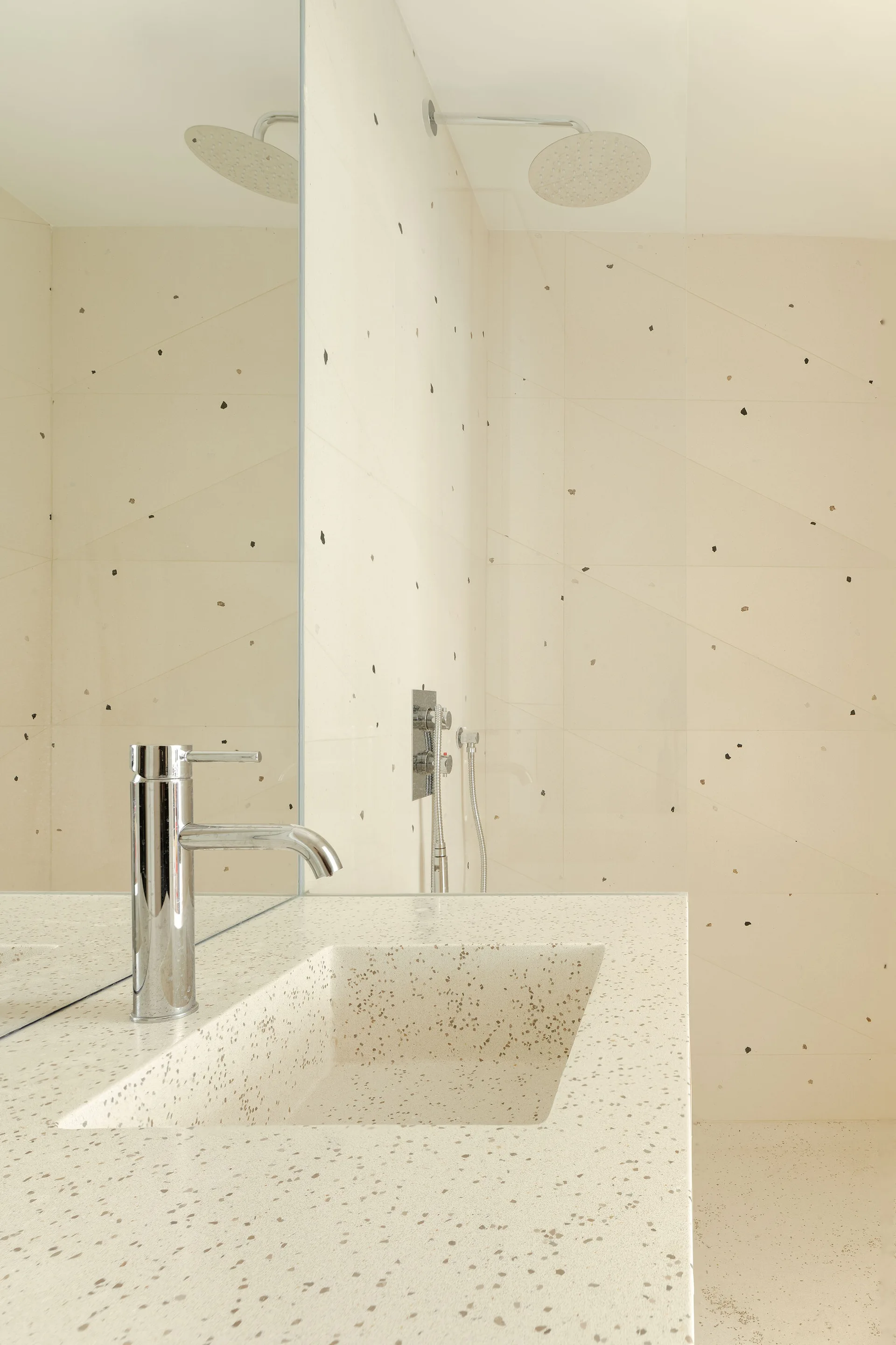 A cream terrazzo bathroom vanity with an integrated sink, a polished chrome faucet, and a background wall mirror reflecting the shower area.