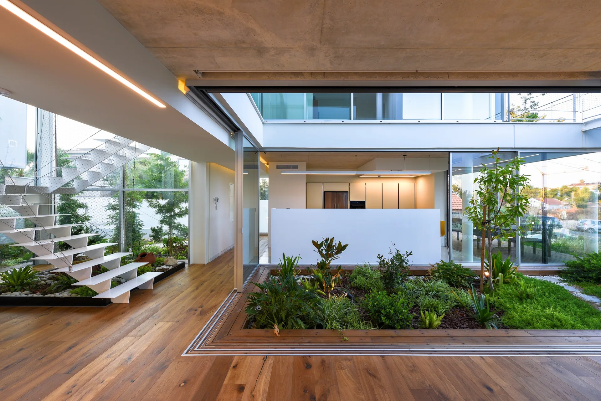 A modern residential interior features a central indoor garden courtyard with green plants, sliding glass doors, and a white floating staircase.