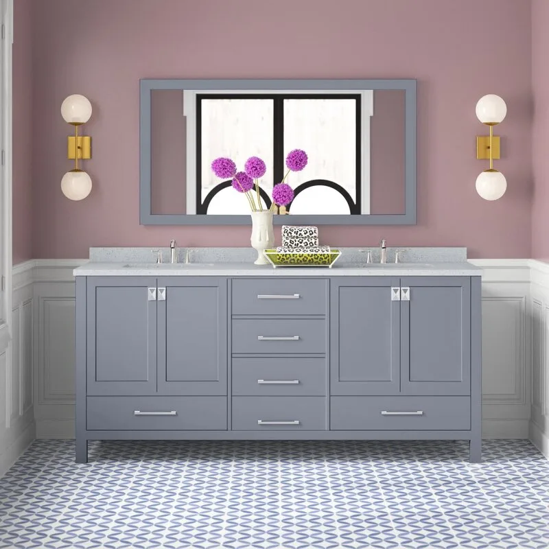A grey double bathroom vanity is set against a mauve wall with white wainscoting, flanked by two brass globe sconces over a patterned tile floor.