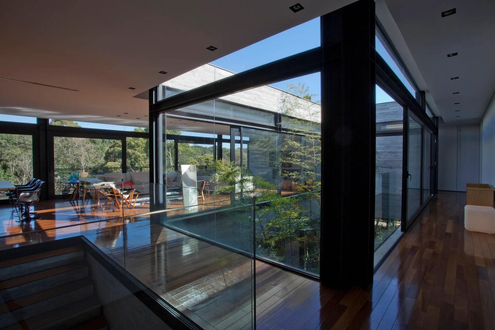 A modern home interior features polished wood floors, black steel frames, and floor-to-ceiling glass walls surrounding an open central courtyard.