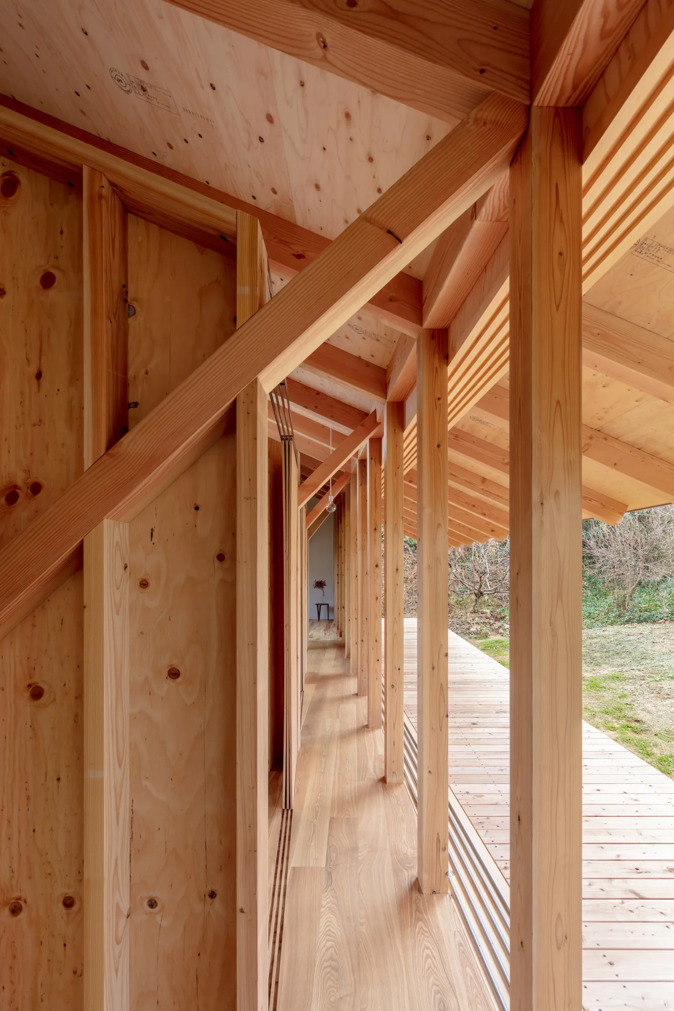 A long corridor built with light-colored plywood walls and exposed timber framing next to a wooden deck.