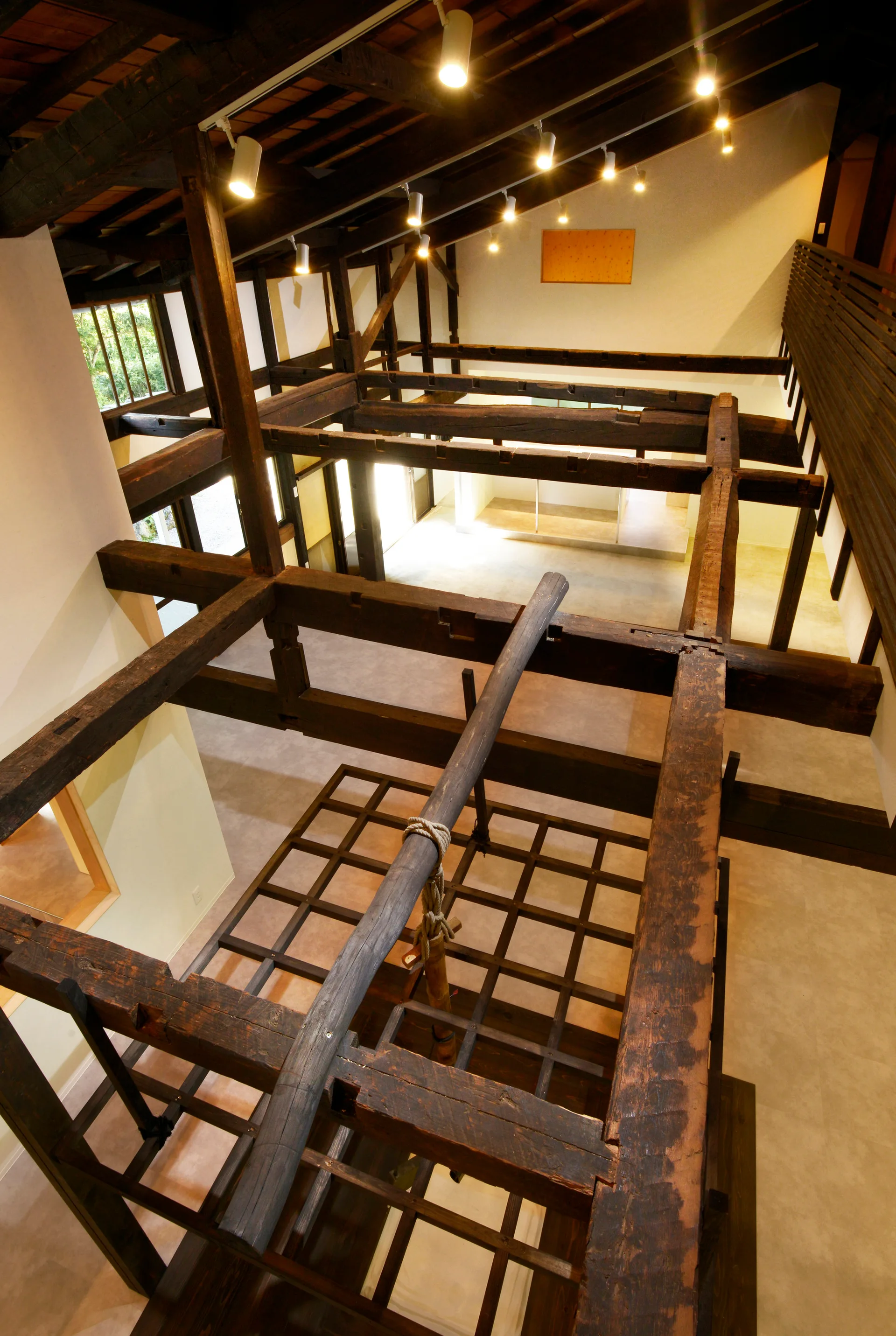 A high-angle view looking down through a double-height loft featuring dark exposed timber beams, white walls, and track lighting.