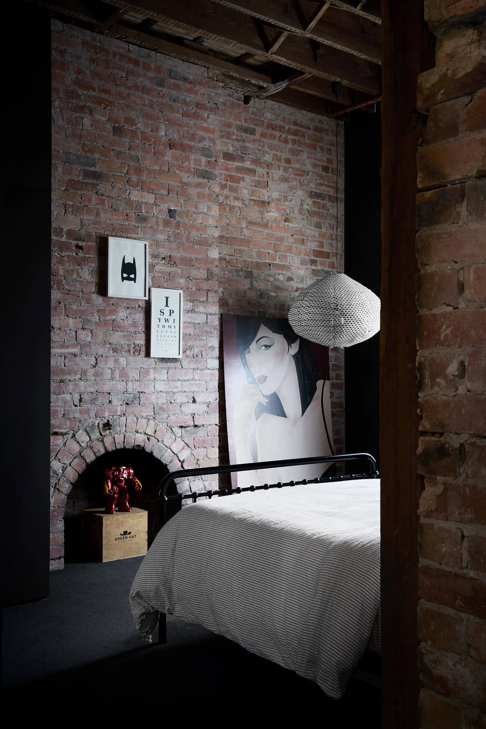 An industrial bedroom with an exposed red brick wall, an arched fireplace hearth, and a black metal-frame bed with striped bedding.
