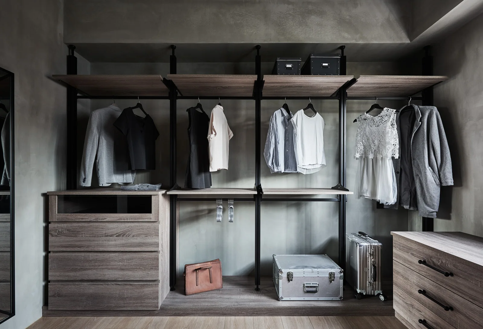 A modern walk-in closet features an open wooden shelving system with black metal frames and matching wood drawer units against textured grey walls.