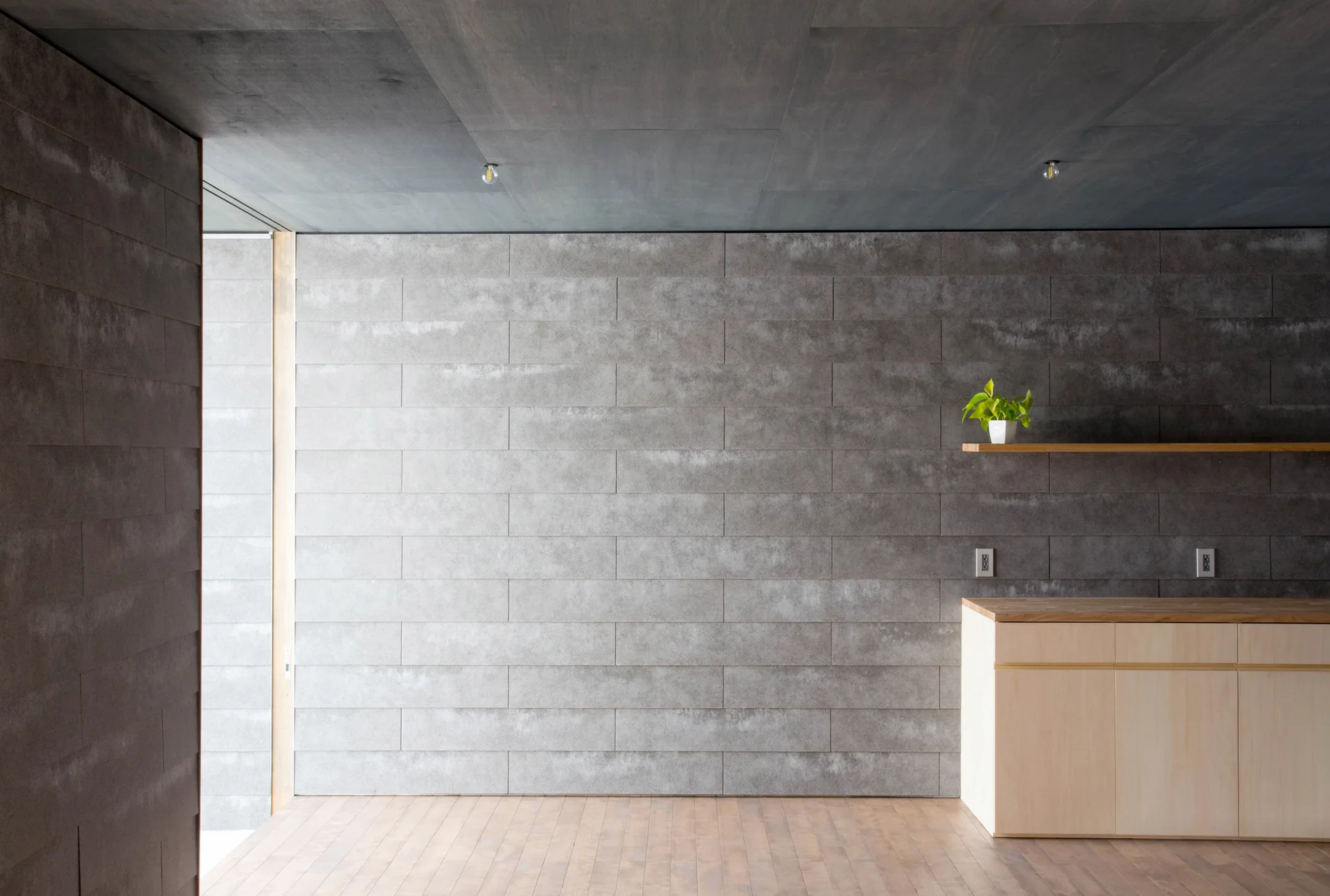 A minimalist room featuring a grey stone tiled wall, a dark wood ceiling, and a light wood base cabinet with a matching floating shelf.