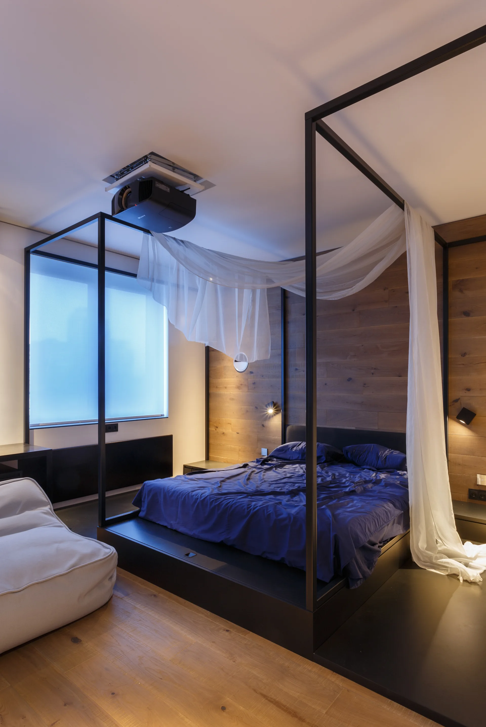 A minimalist bedroom features a black metal canopy bed with sheer white drapes against a horizontal wood plank accent wall.