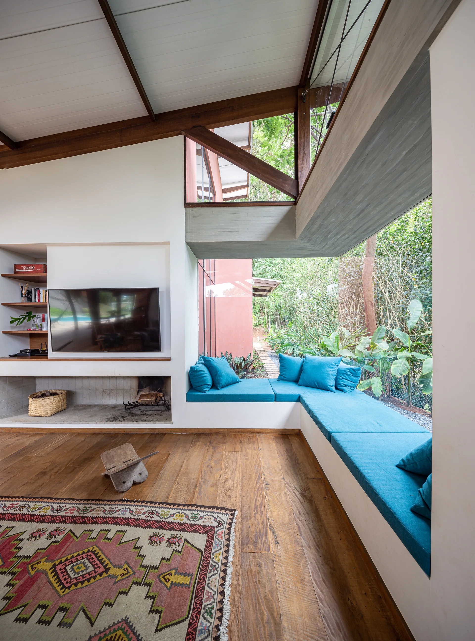 A living room featuring a built-in corner bench with blue cushions beneath large windows overlooking a lush garden.