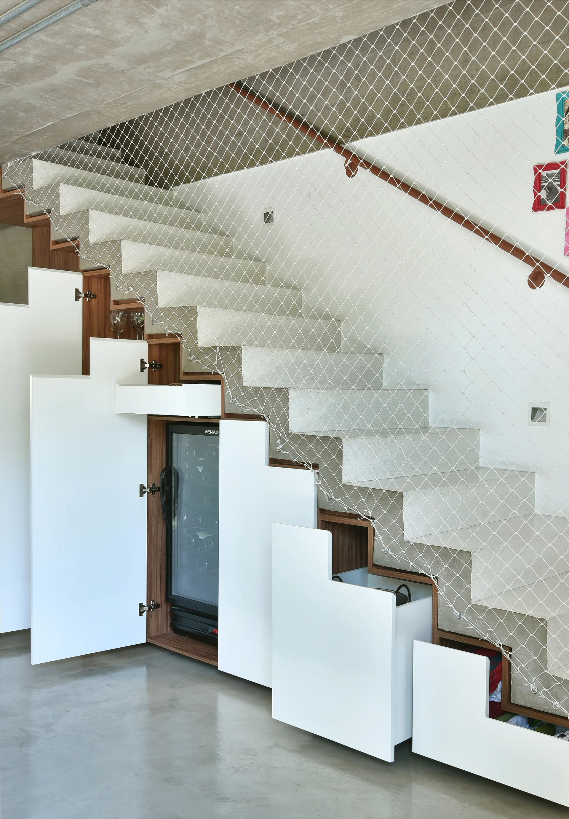 A light stone staircase features built-in white step-shaped cabinets, an integrated wine cooler, and a white mesh safety net.
