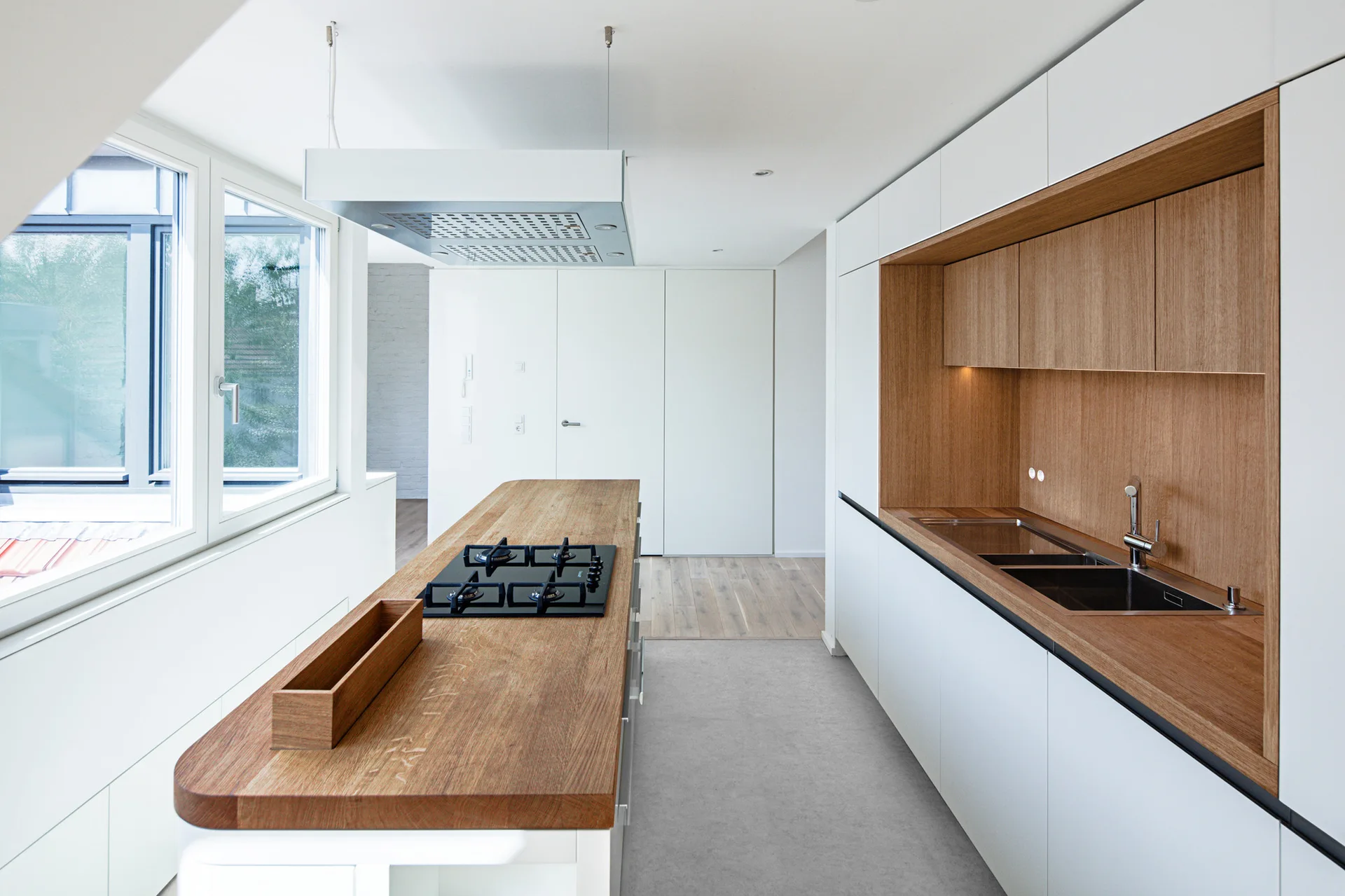 A modern kitchen featuring white flat-panel cabinets with a recessed wood niche, a wood-topped kitchen island, and grey flooring.