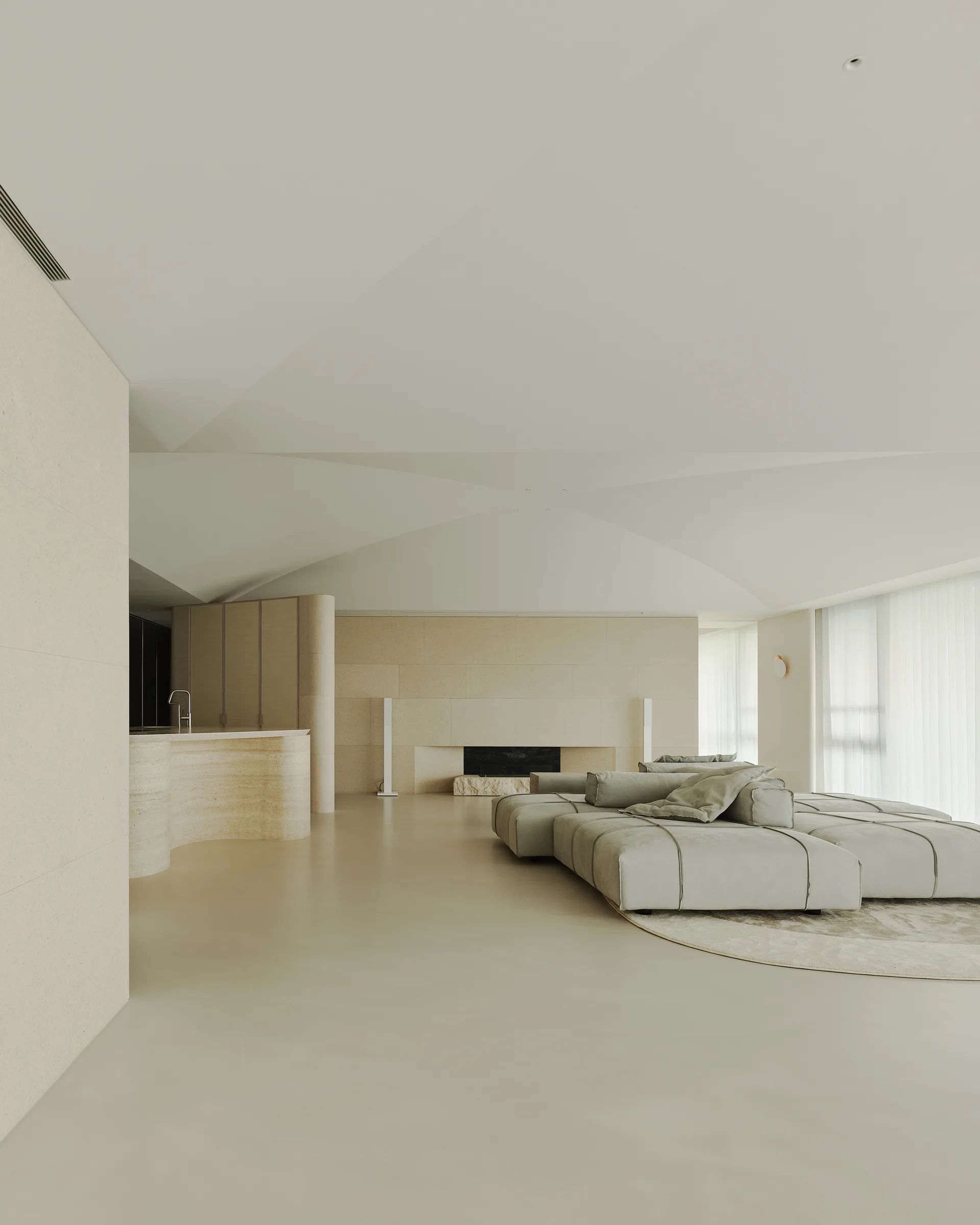 A minimalist beige living room featuring a low-profile modular sectional sofa, a vaulted ceiling, and a stone-clad wall with a fireplace.