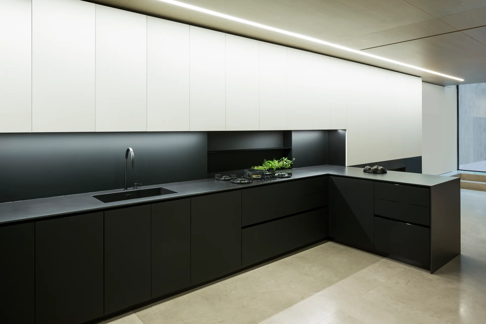 A modern L-shaped kitchen features matte black lower cabinets, white upper cabinets, a dark countertop with an undermount sink, and integrated LED lighting.