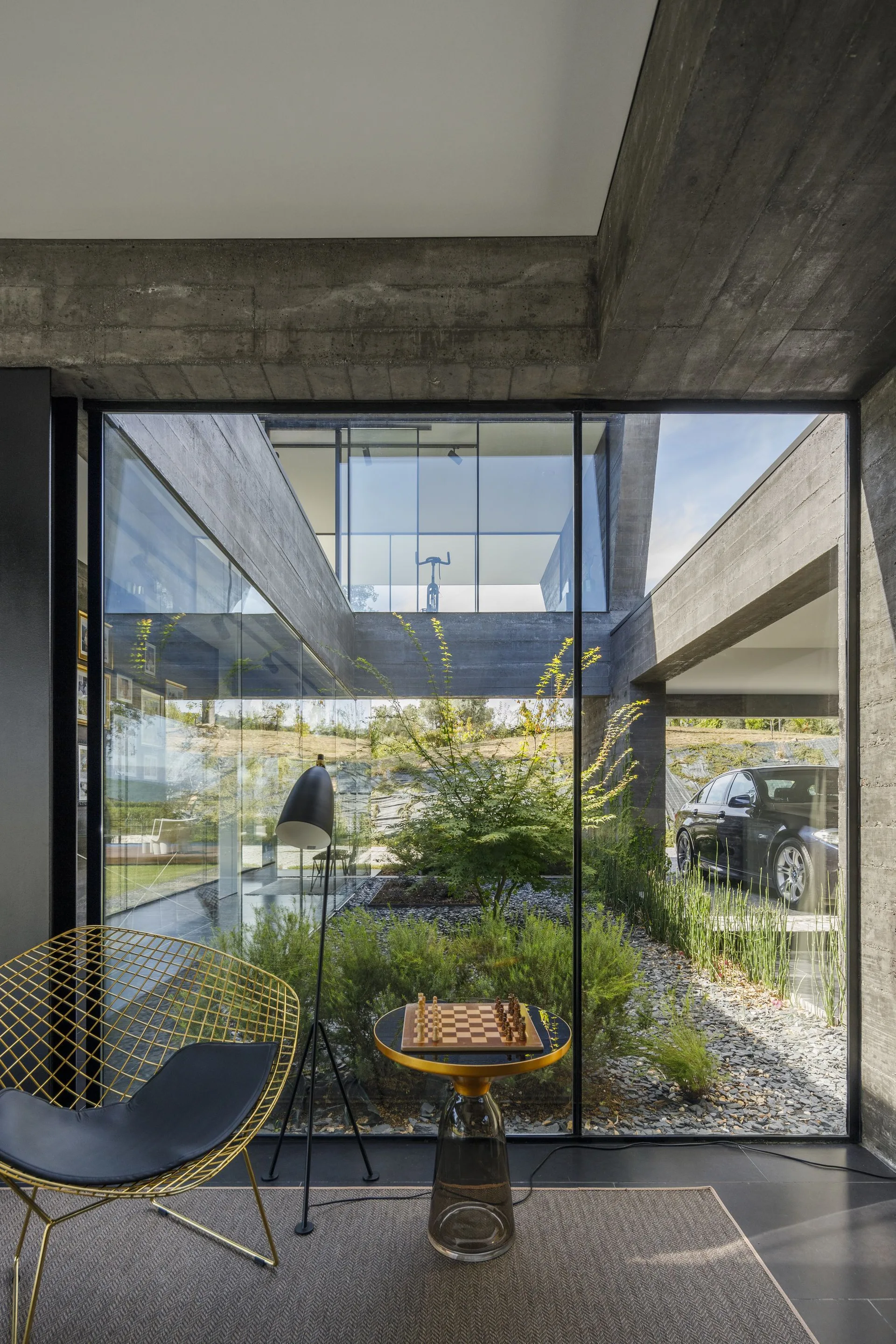 A modern lounge area with a gold wire chair and chess table next to large glass walls looking out at a landscaped concrete courtyard.