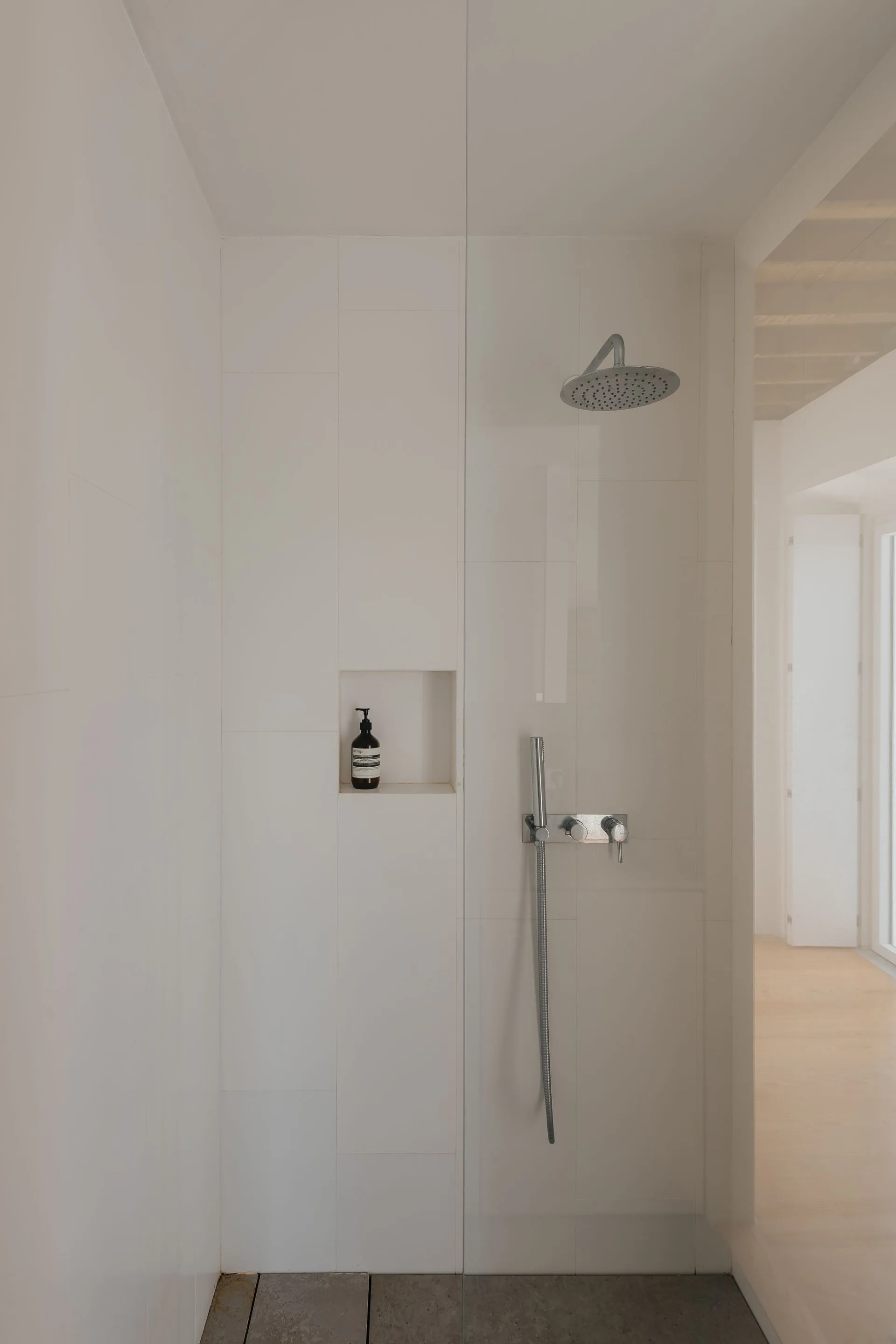 A minimalist walk-in shower featuring large-format white tiles, a built-in recessed storage niche, and chrome fixtures.