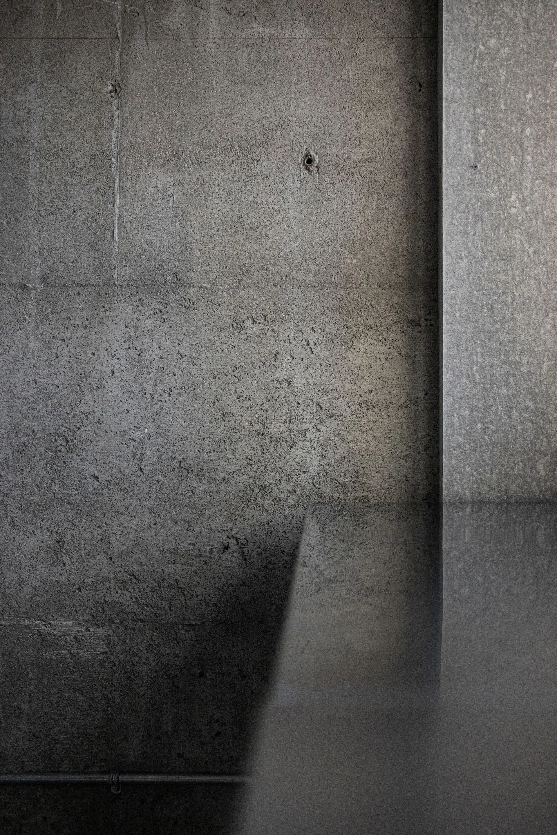 A textured gray concrete wall with a matte finish stands behind a dark, highly polished horizontal countertop.