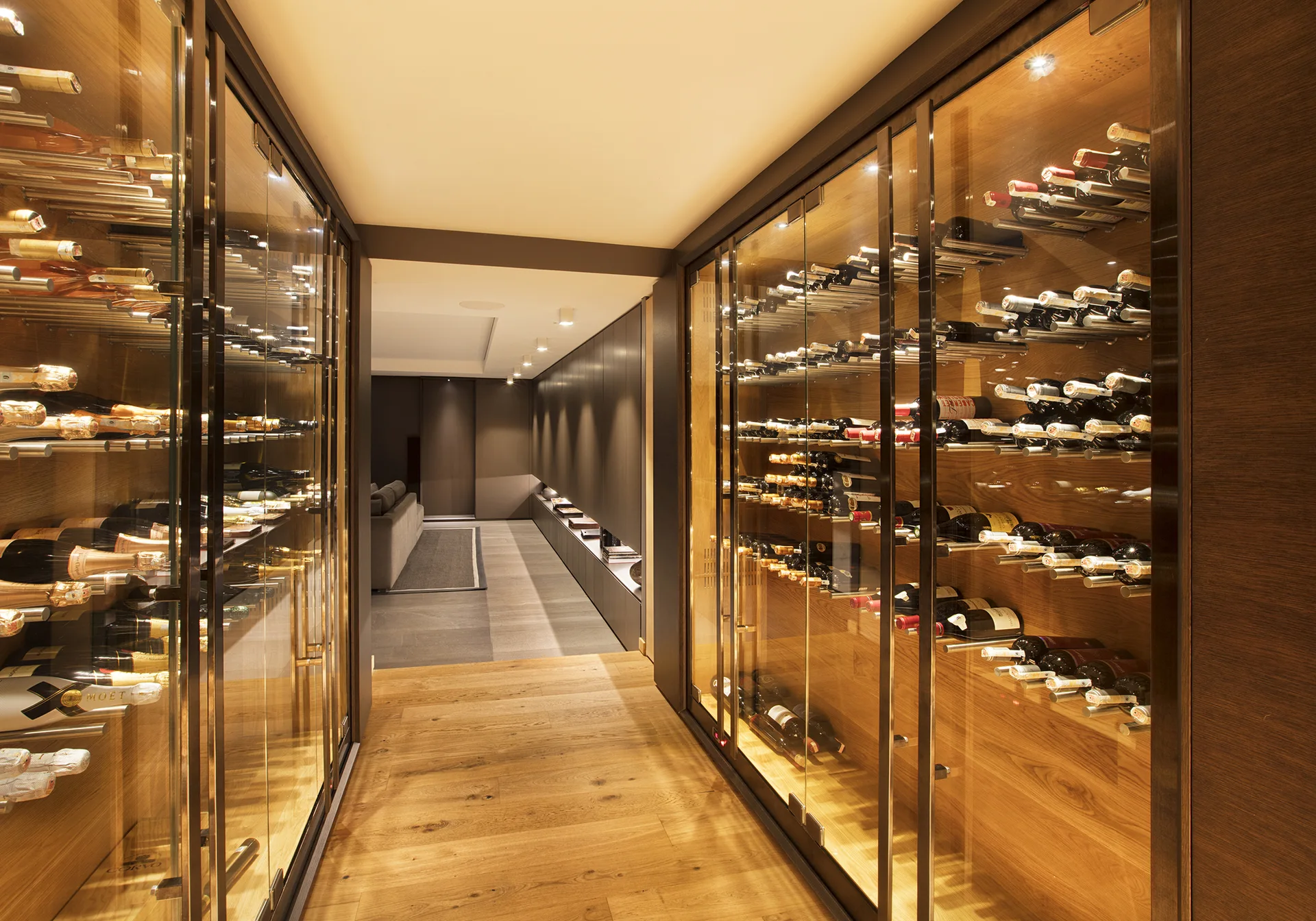 A wood-paneled hallway features built-in glass wine cabinets with interior lighting, leading to a contemporary seating area.
