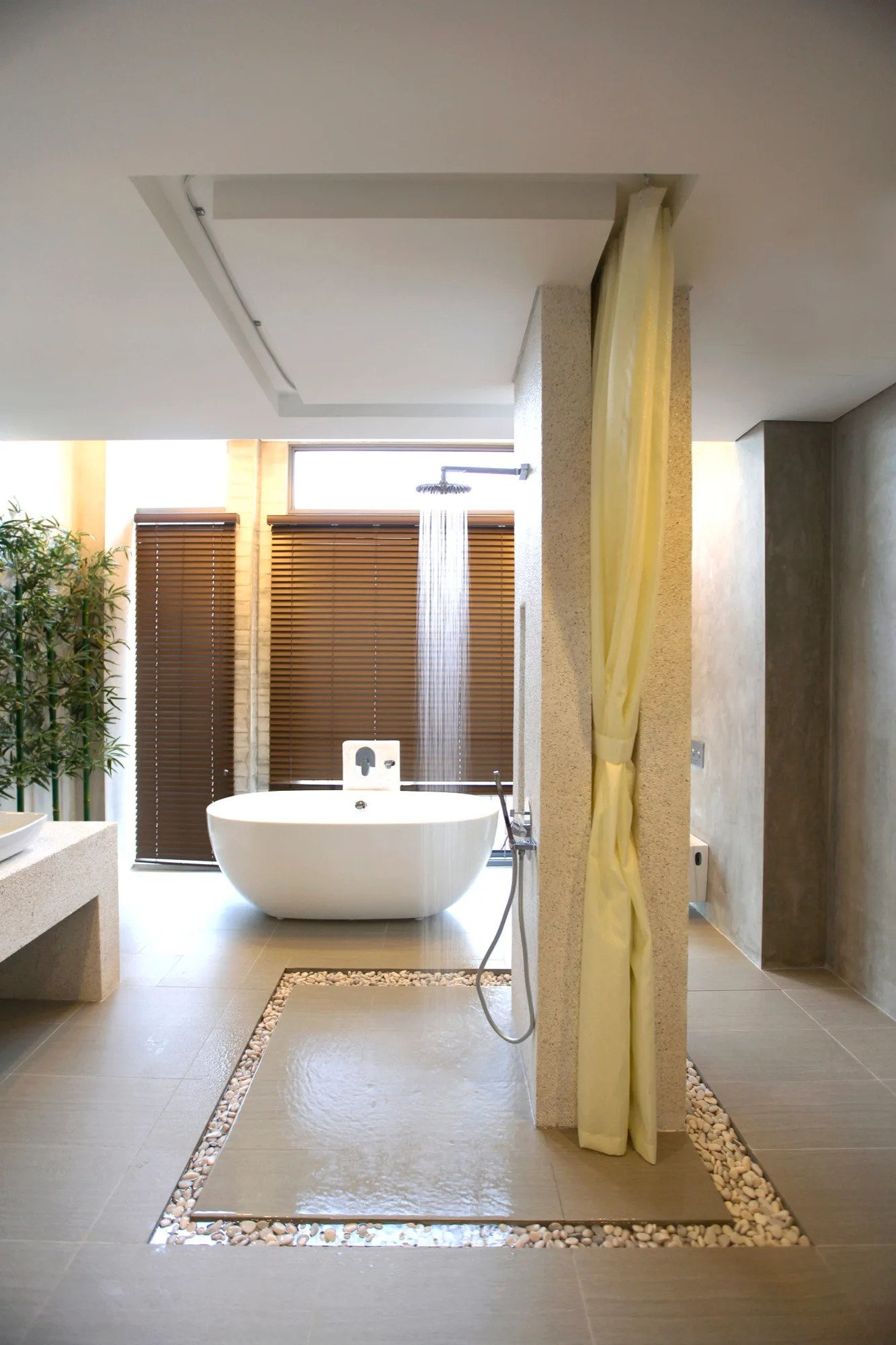 A spacious beige bathroom featuring an open walk-in shower with running water, a river pebble floor border, and a freestanding tub.