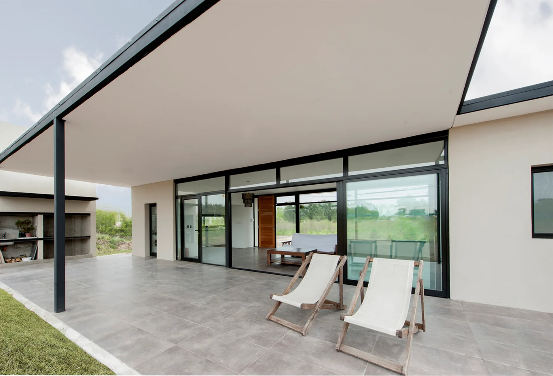 A modern covered patio features gray floor tiles, two white fabric deck chairs, and large black-framed sliding glass doors leading to the interior.