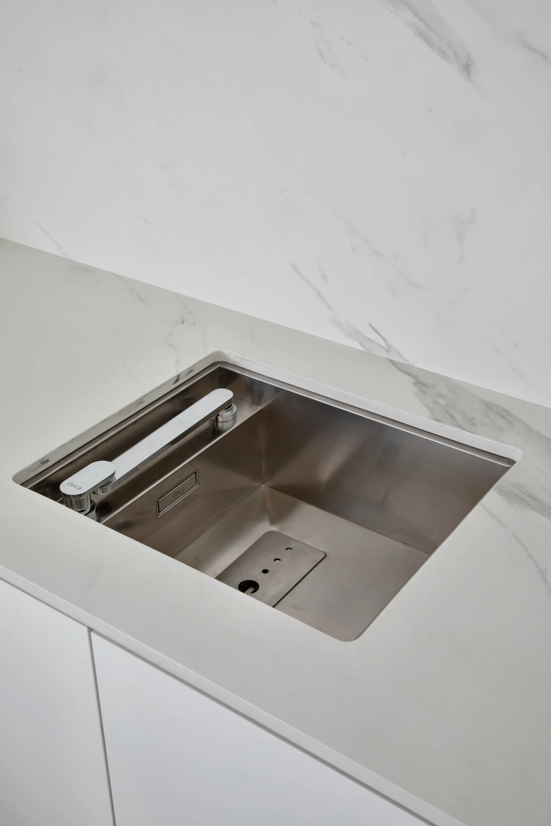 A stainless steel undermount kitchen sink with a low-profile faucet is set into a white veined marble countertop with matching backsplash.