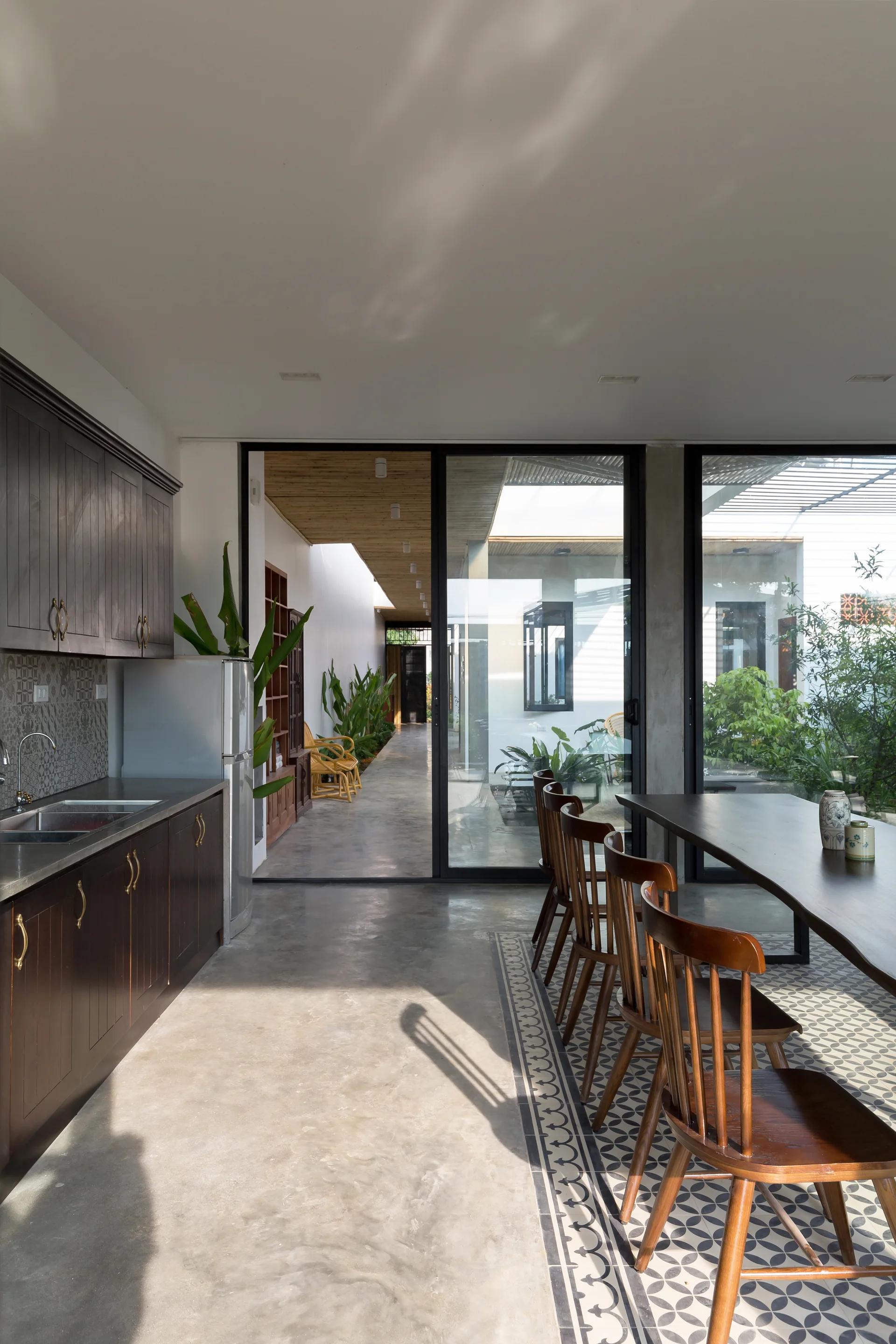 A bright dining area features a dark wood table set on geometric tiled floor inlay next to large glass doors opening to a garden hallway.