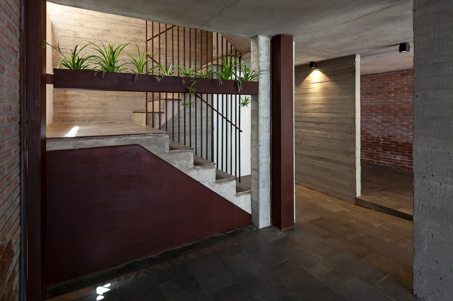 An industrial concrete staircase features a rusted metal railing and a built-in planter trough with green spider plants.