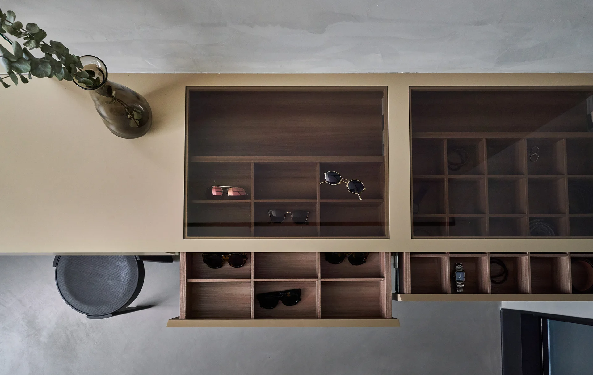 An overhead view of a custom beige dressing table featuring glass-topped drawers with wooden divided compartments for storing sunglasses.