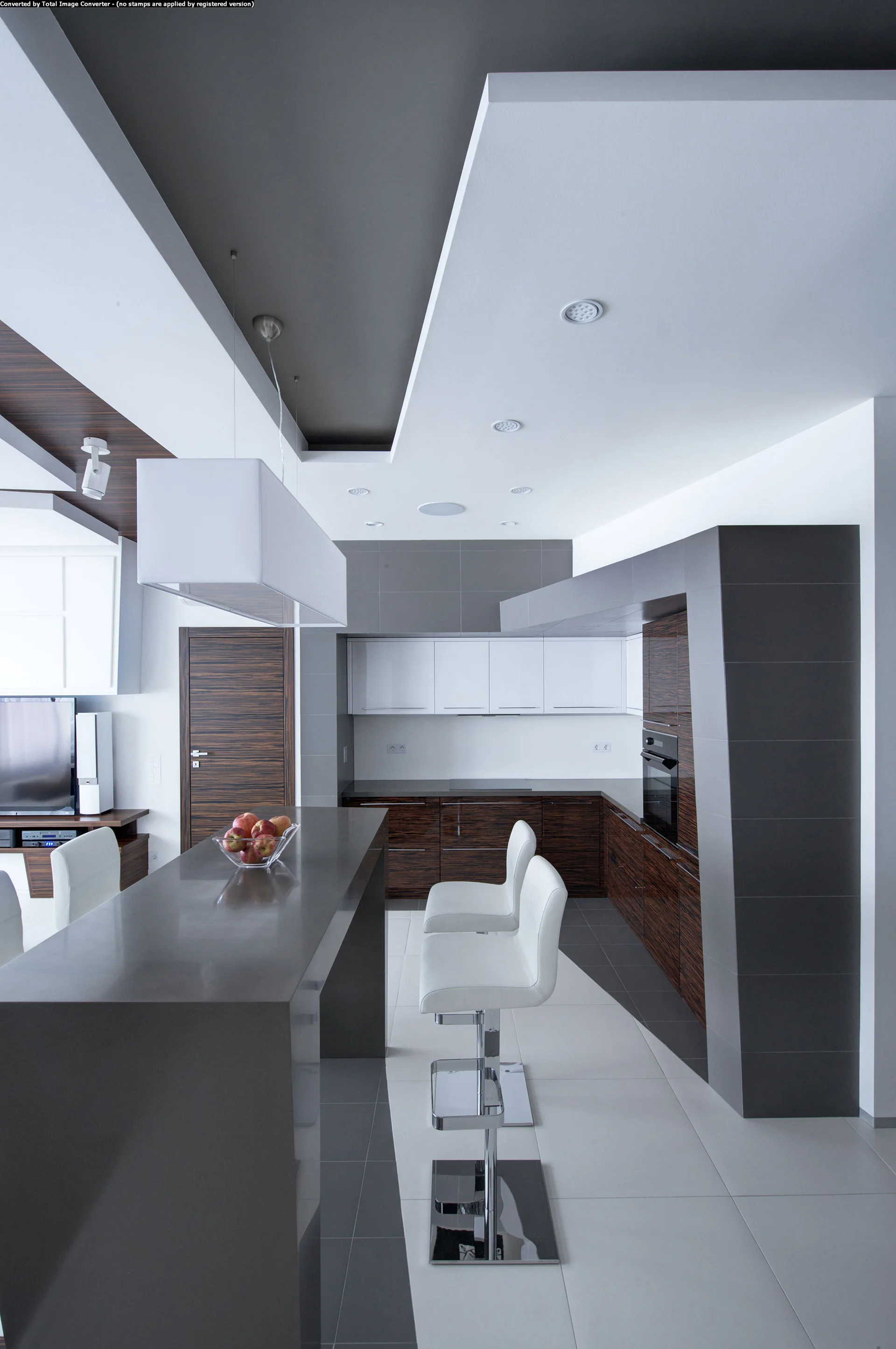 A modern kitchen featuring a dark grey island with white bar stools, dark wood grain lower cabinets, and a white layered ceiling with recessed lighting.