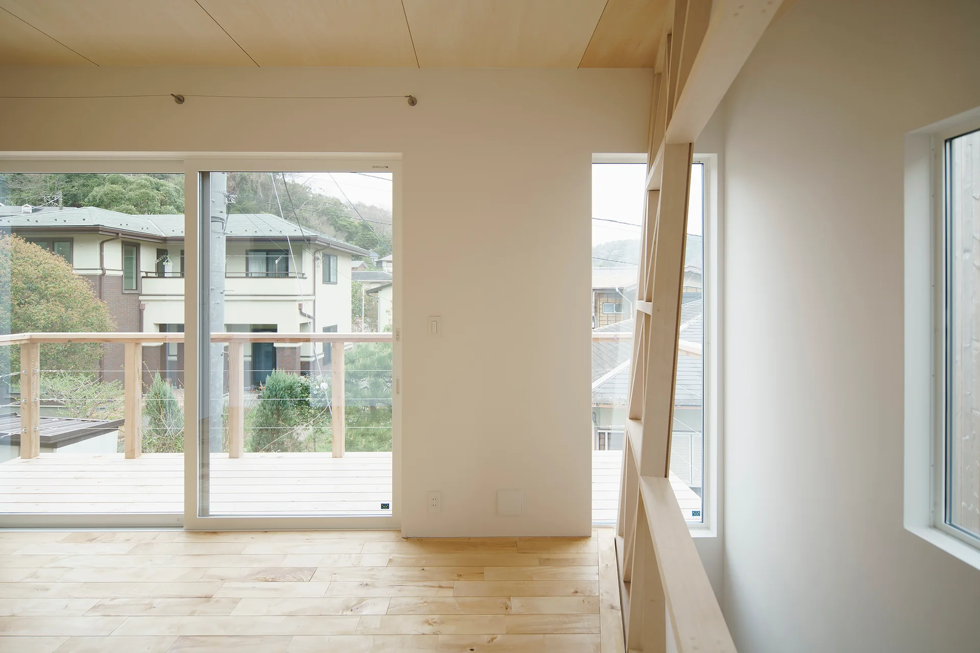 A minimalist room features light wood floors, a matching paneled wood ceiling, white walls, and a large sliding glass door opening to a deck.