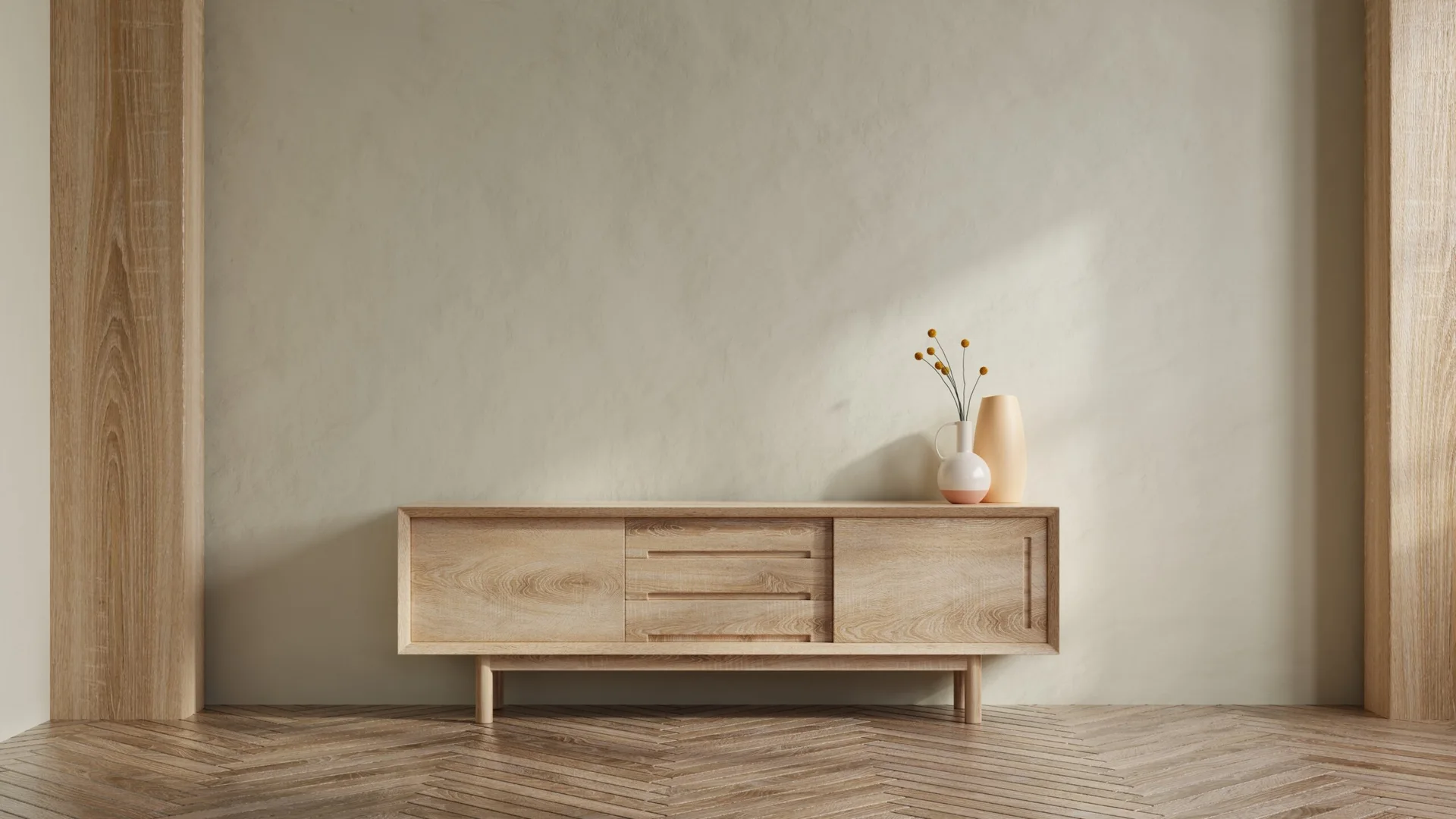 A light oak credenza stands against a textured beige plaster wall on a classic herringbone parquet floor with two ceramic vases on top.