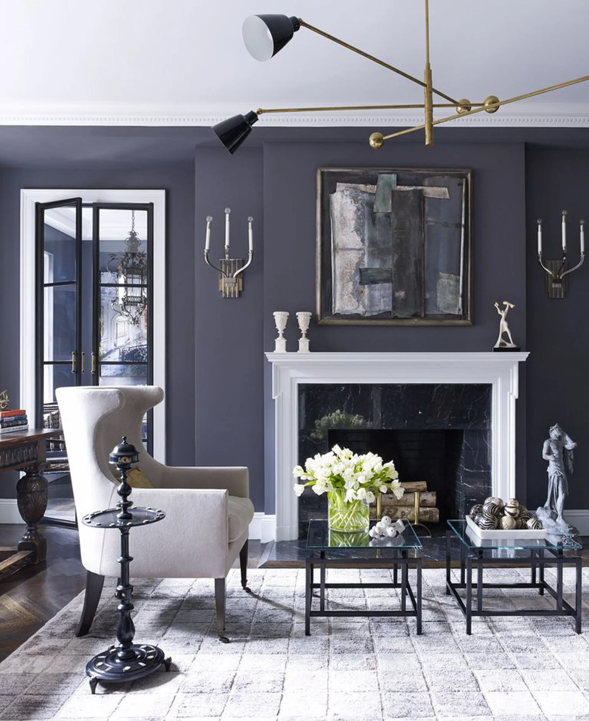 A living room with charcoal walls, a white mantel on a black marble fireplace, a cream wingback chair, and a brass ceiling light.