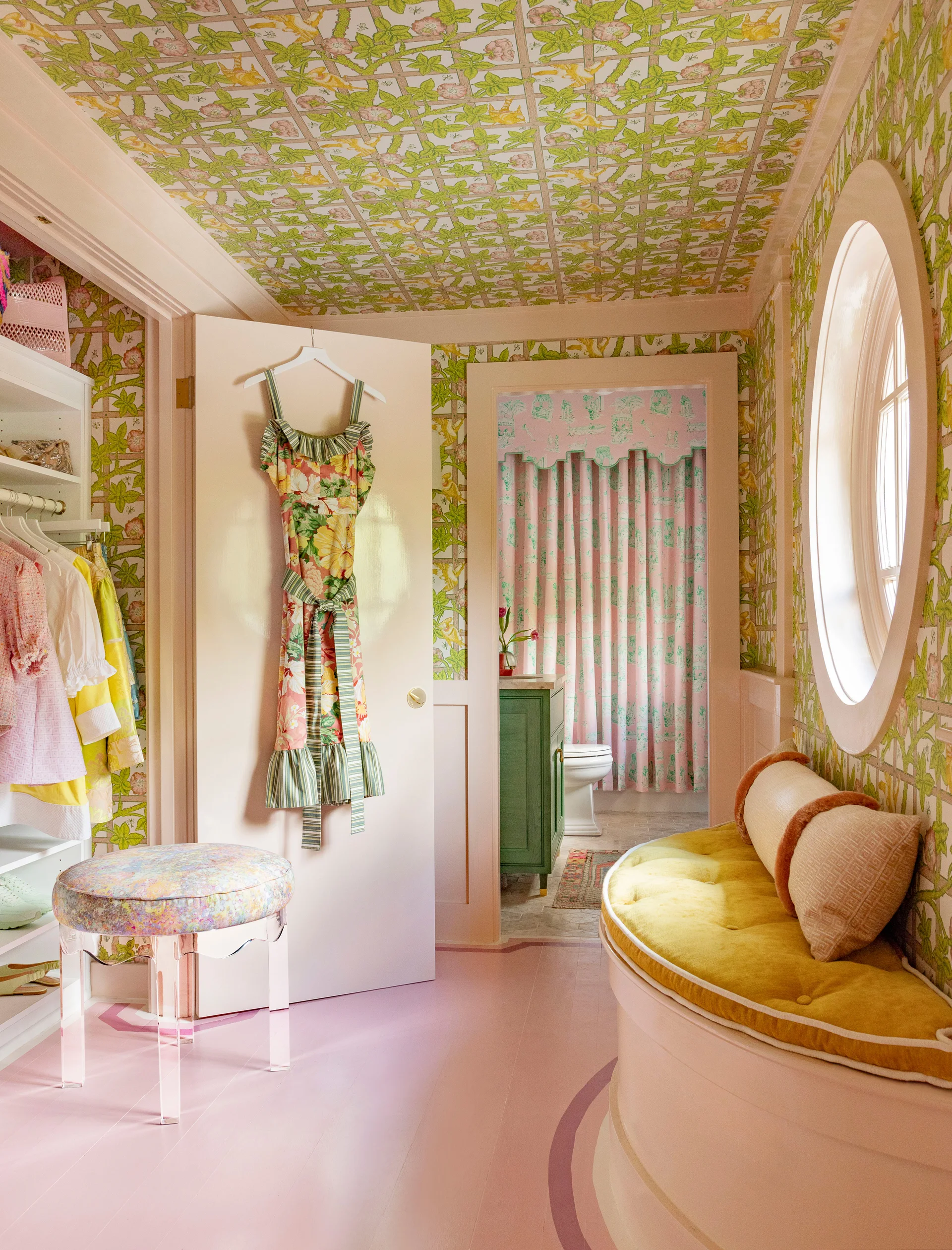 A whimsical dressing room featuring green trellis wallpaper on the walls and ceiling, a curved window bench, and a pink painted floor.