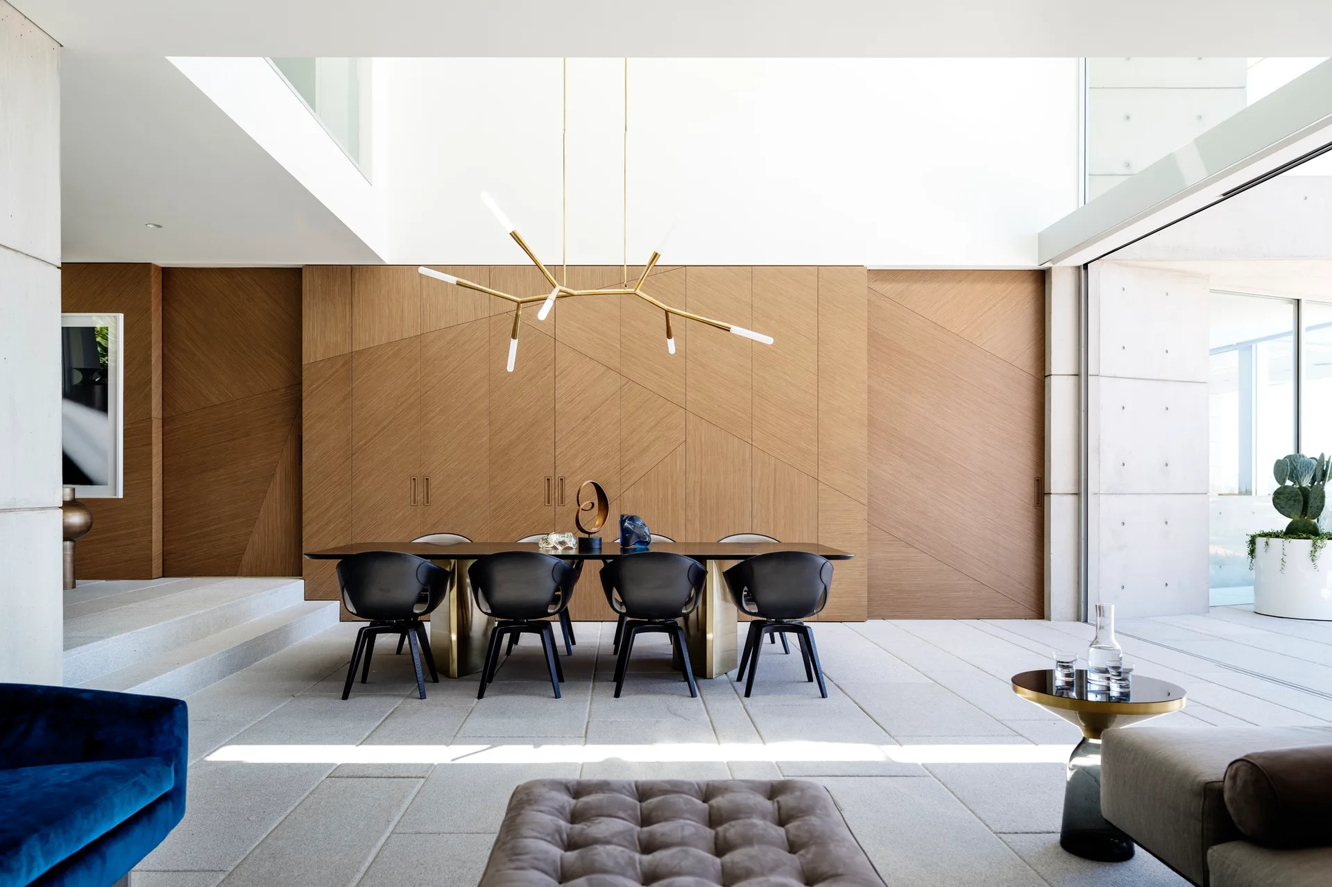A modern dining area featuring a dark wood table with black chairs positioned against a geometric wood-paneled wall under a gold branching pendant light.