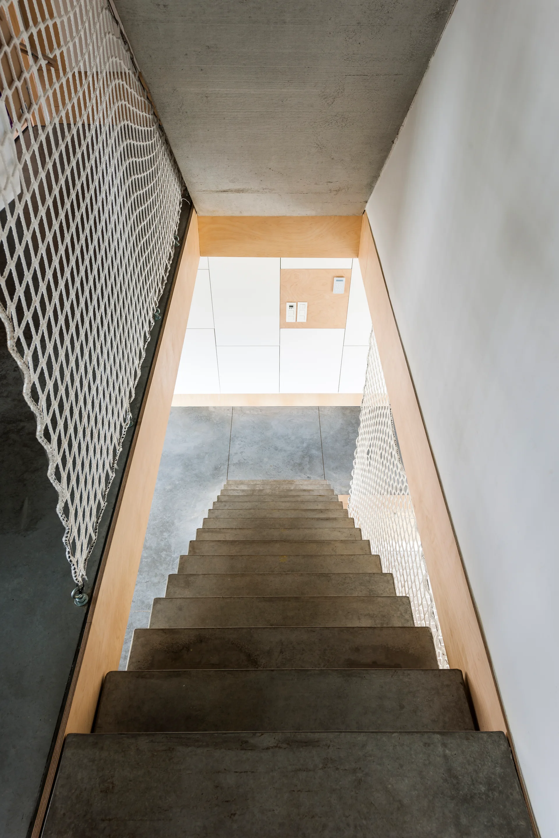 Looking down a concrete staircase with light plywood trim on the sides and white rope safety netting serving as a handrail guard.