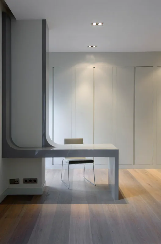 A minimalist home office features a gray cantilevered desk integrated into a wall column, a simple chair, and floor-to-ceiling flat-panel cabinets.