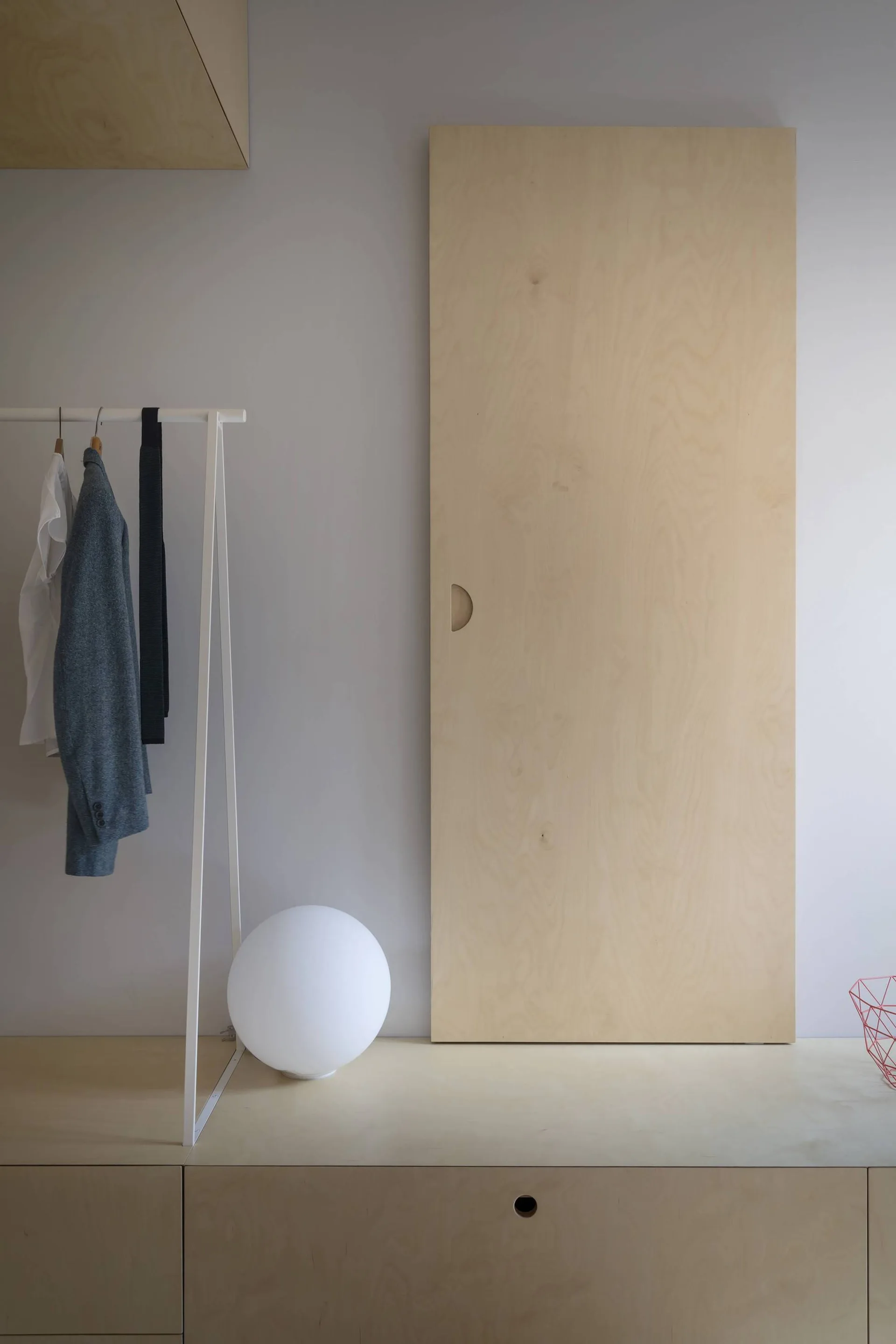 A light plywood sliding door and low built-in cabinets stand next to a white metal clothing rack and a glowing spherical globe lamp.
