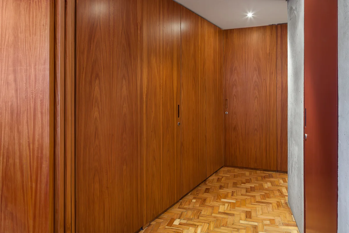 A minimalist hallway featuring floor-to-ceiling warm wood paneling, a herringbone parquet floor, and an exposed concrete wall on the side.