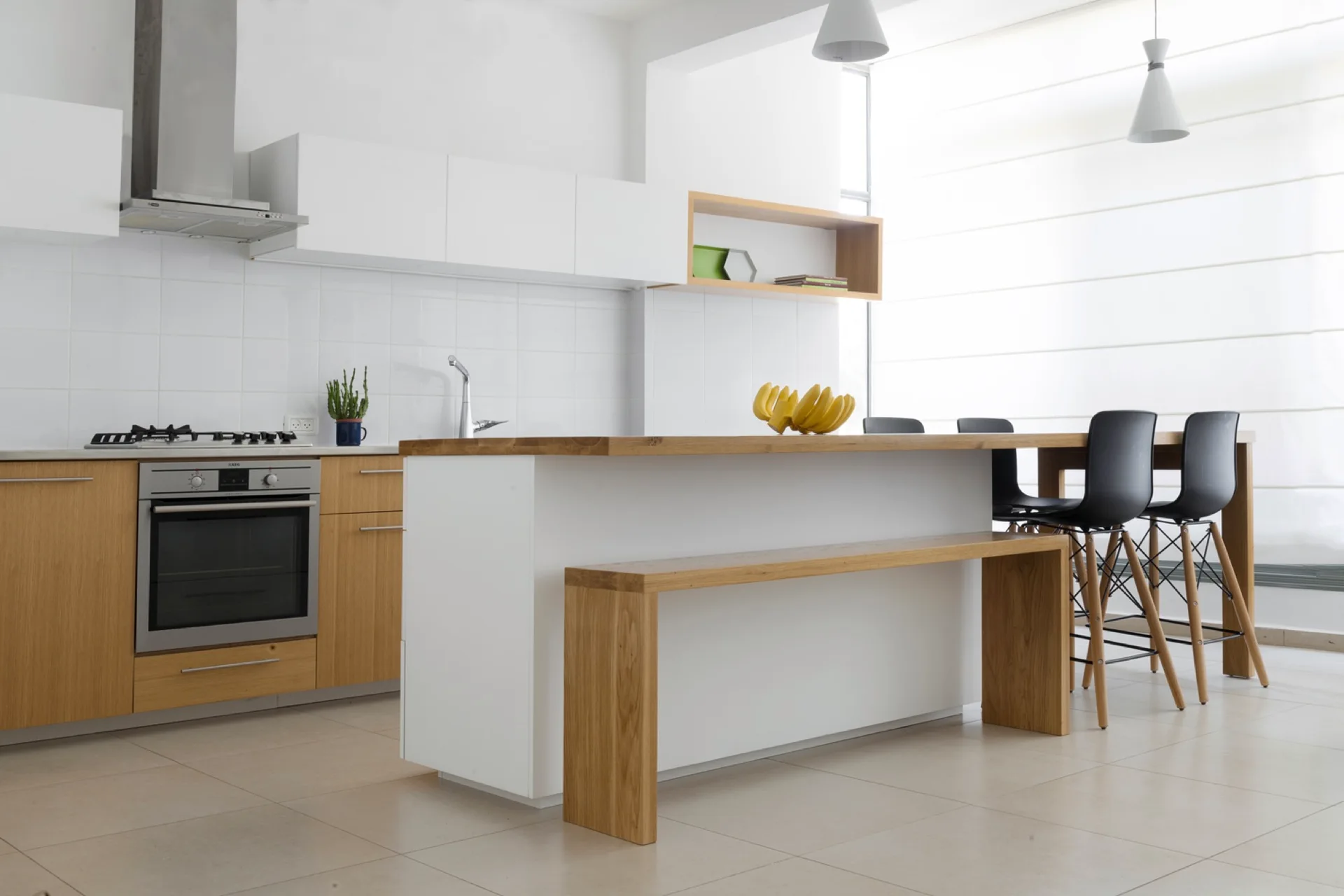 A modern kitchen features white upper cabinets, wood-toned lower cabinets, a central white island with a wood countertop, and black bar stools.