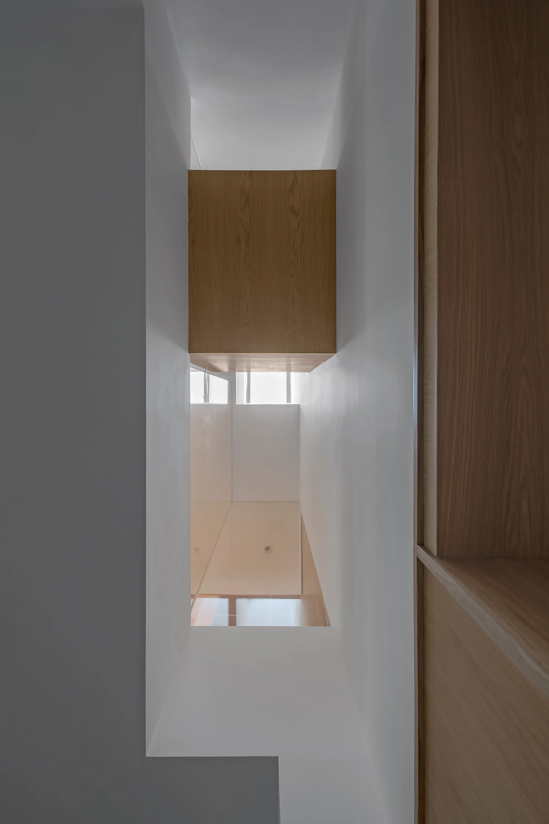 A vertical architectural light well with smooth white plaster walls, a skylight above, and integrated wood-toned cabinets along one side.
