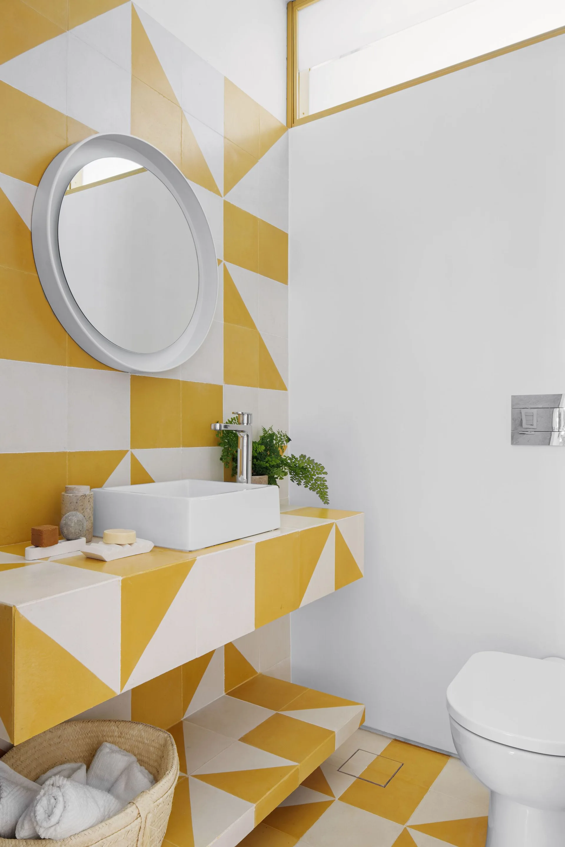 A modern bathroom features bold yellow and white geometric tile wrapping the wall, floor, and floating vanity beneath a round mirror.