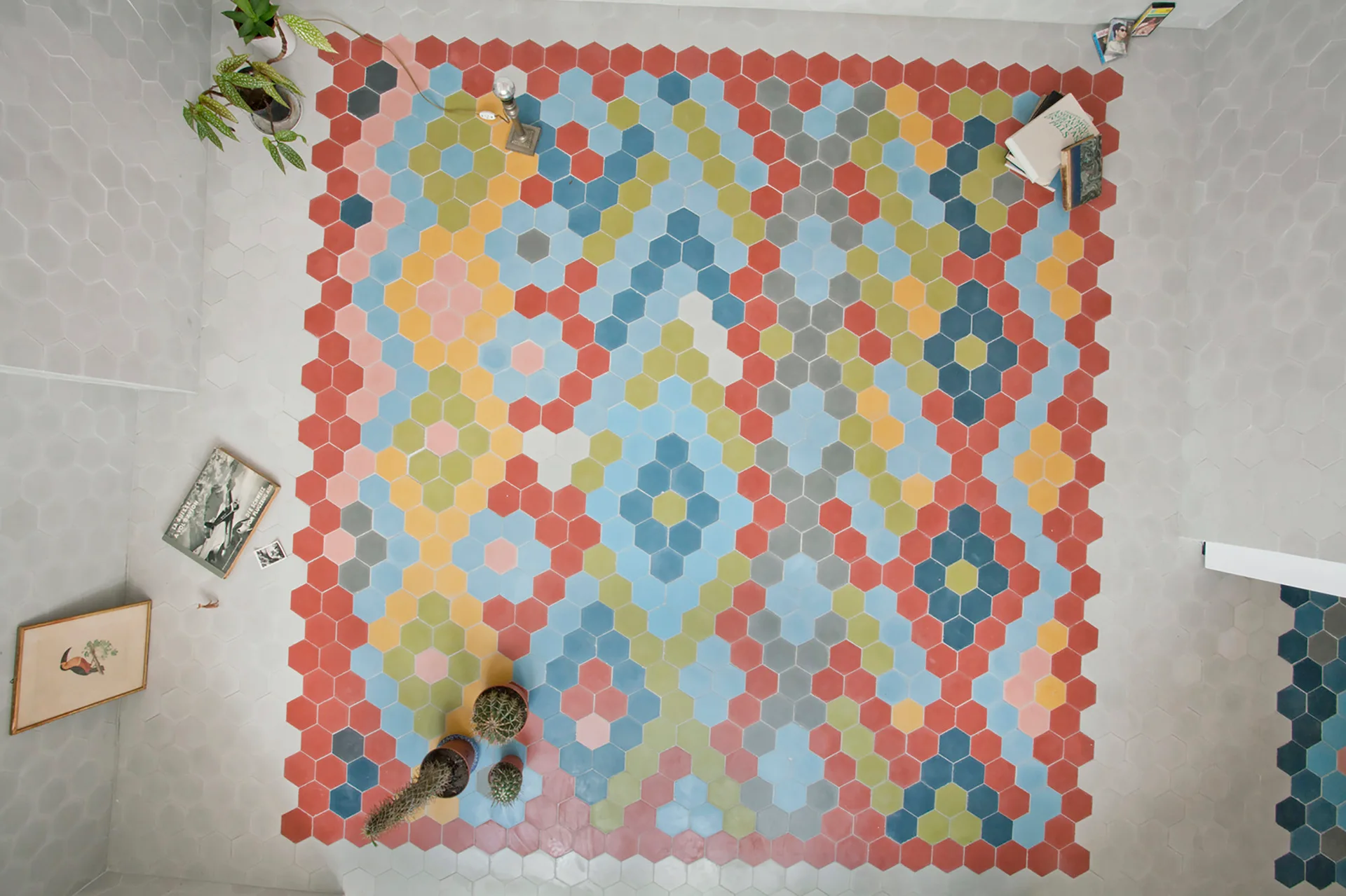 An overhead view of a floor covered in colorful hexagonal tiles arranged in a geometric pattern and surrounded by light gray tiles.