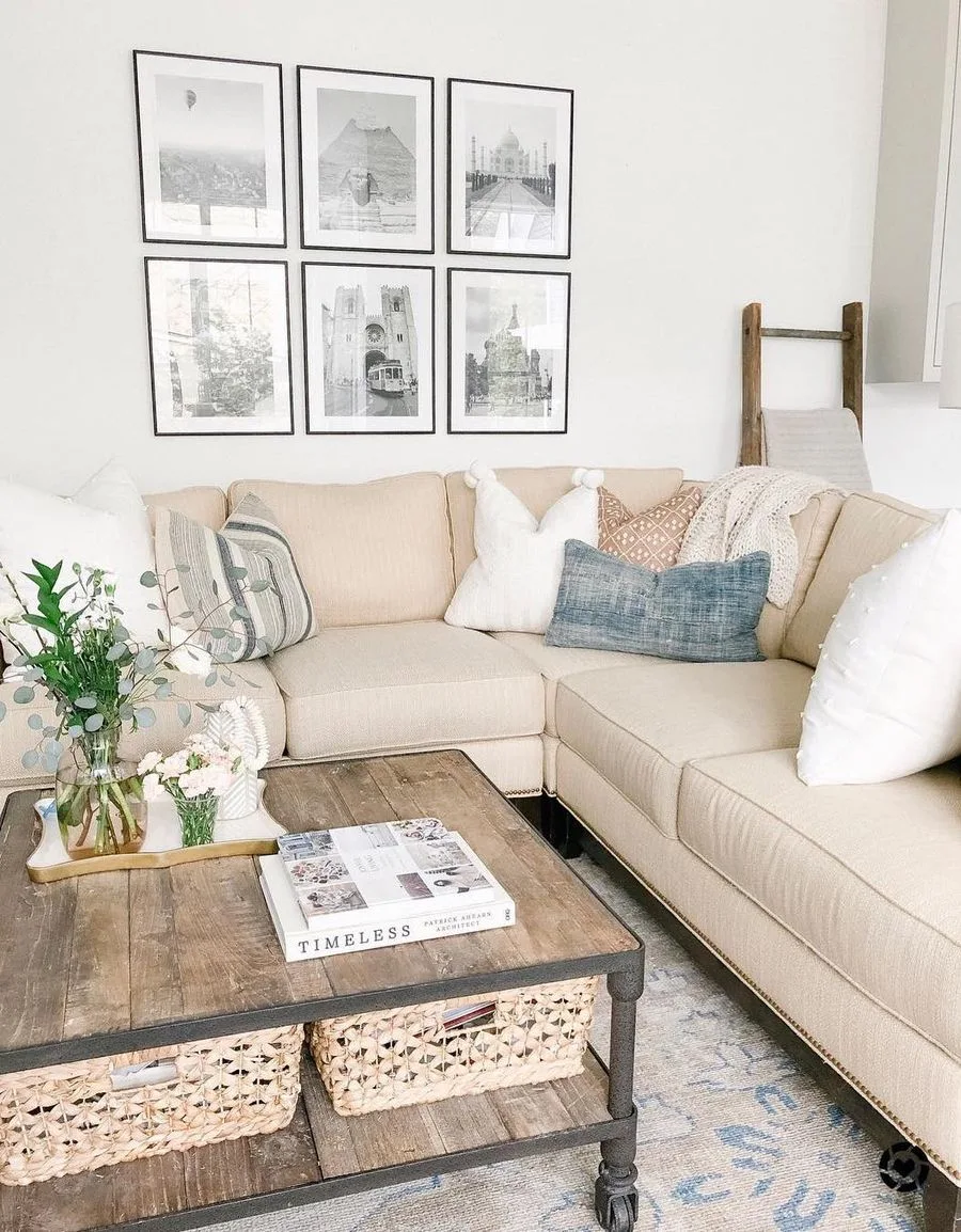 A neutral living room features a beige sectional sofa with patterned throw pillows, a grid of six black-framed pictures, and a rustic wood coffee table.
