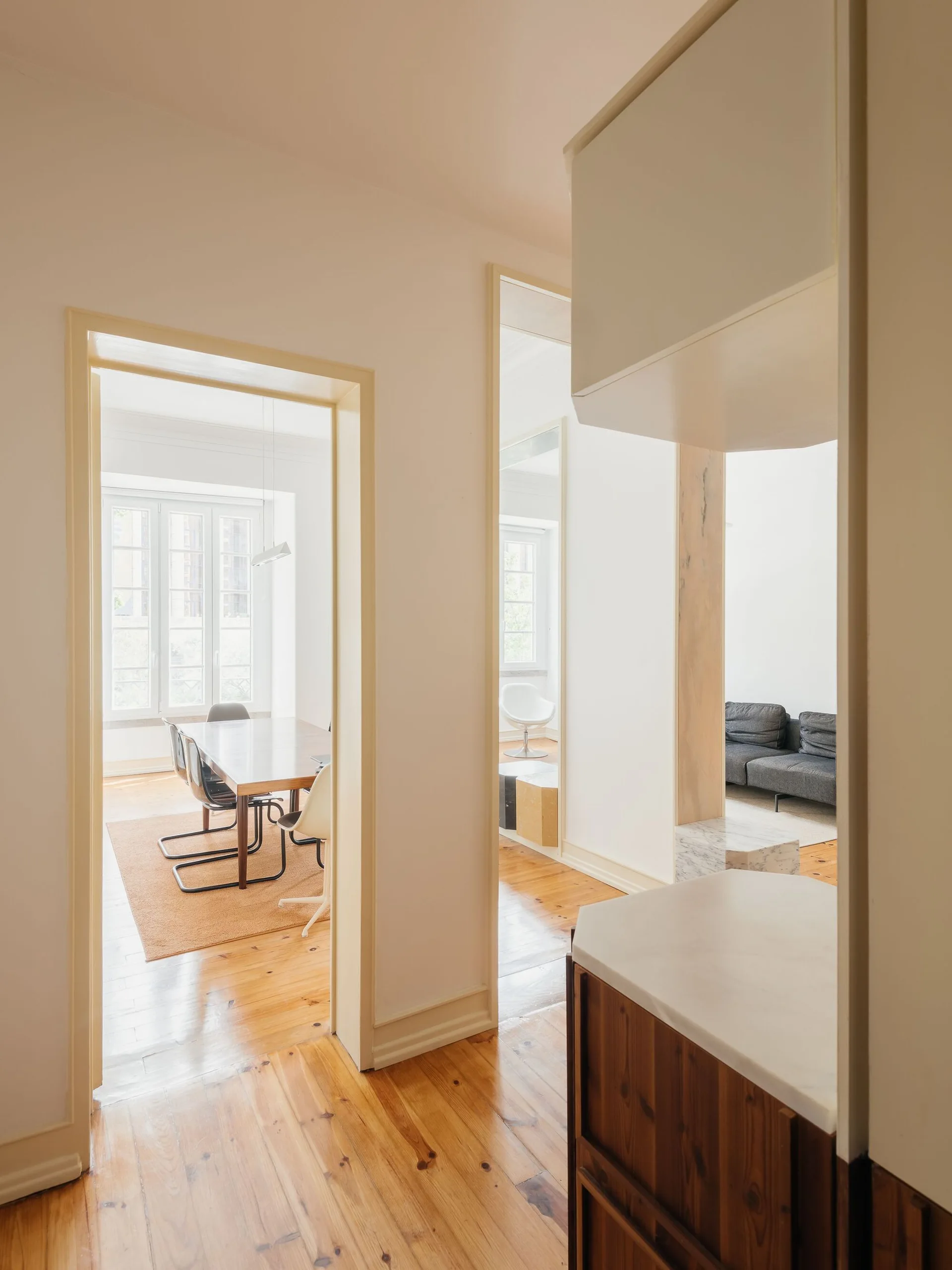A view through open doorways showing a dining room with a wooden table and a living room with a grey sofa, all connected by warm pine flooring.