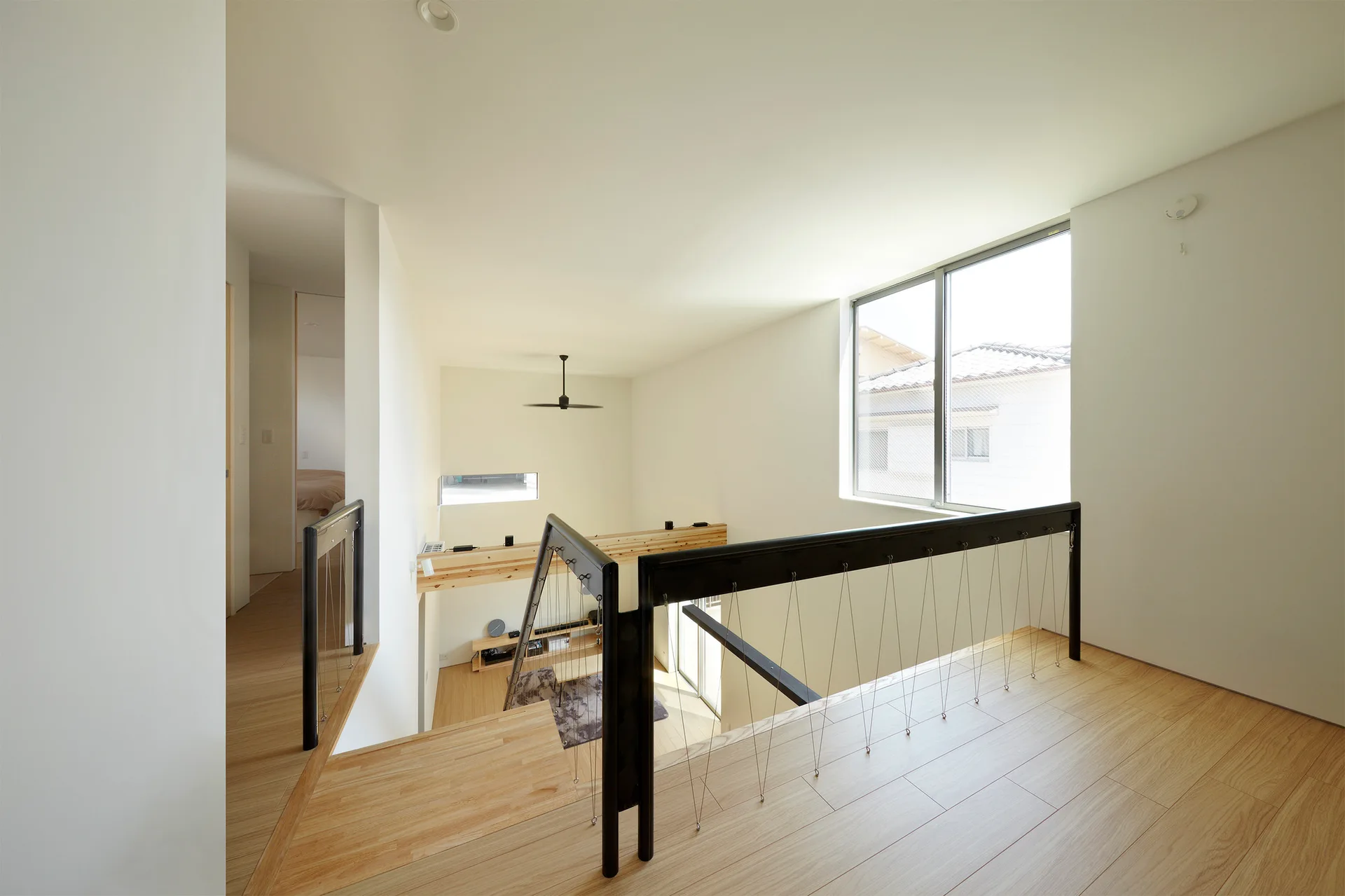 A bright minimalist upper landing features light wood floors and a modern black metal cable railing overlooking a lower level.