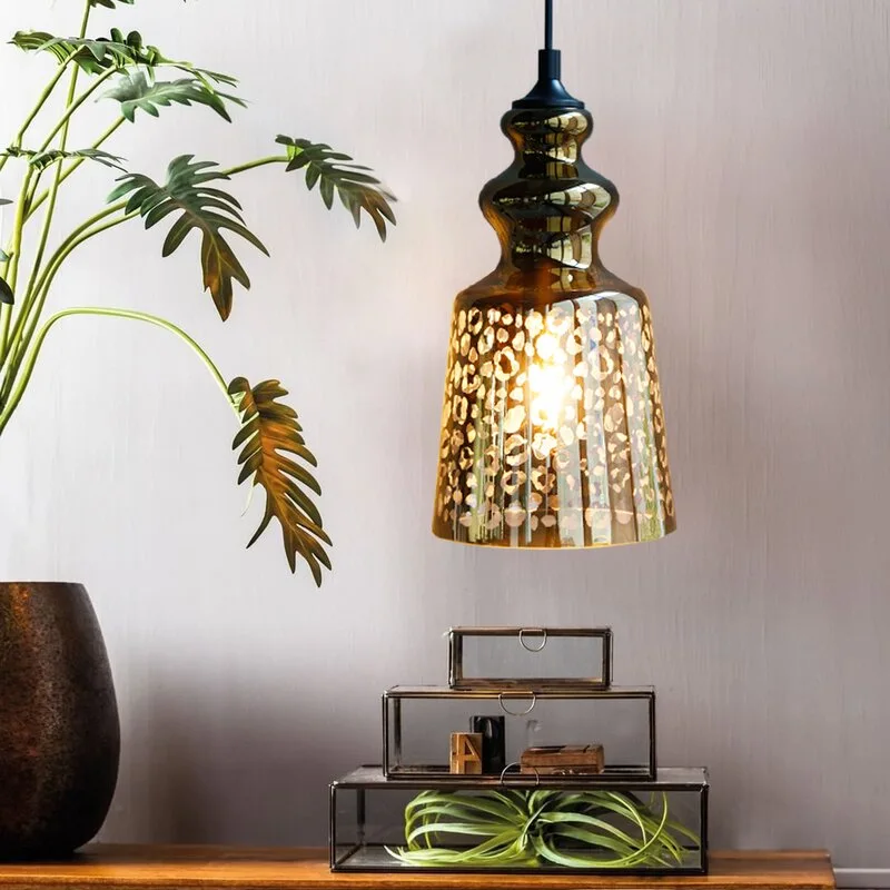 An amber glass pendant lamp with a leopard print pattern hangs above stacked glass display boxes and a leafy green potted plant.