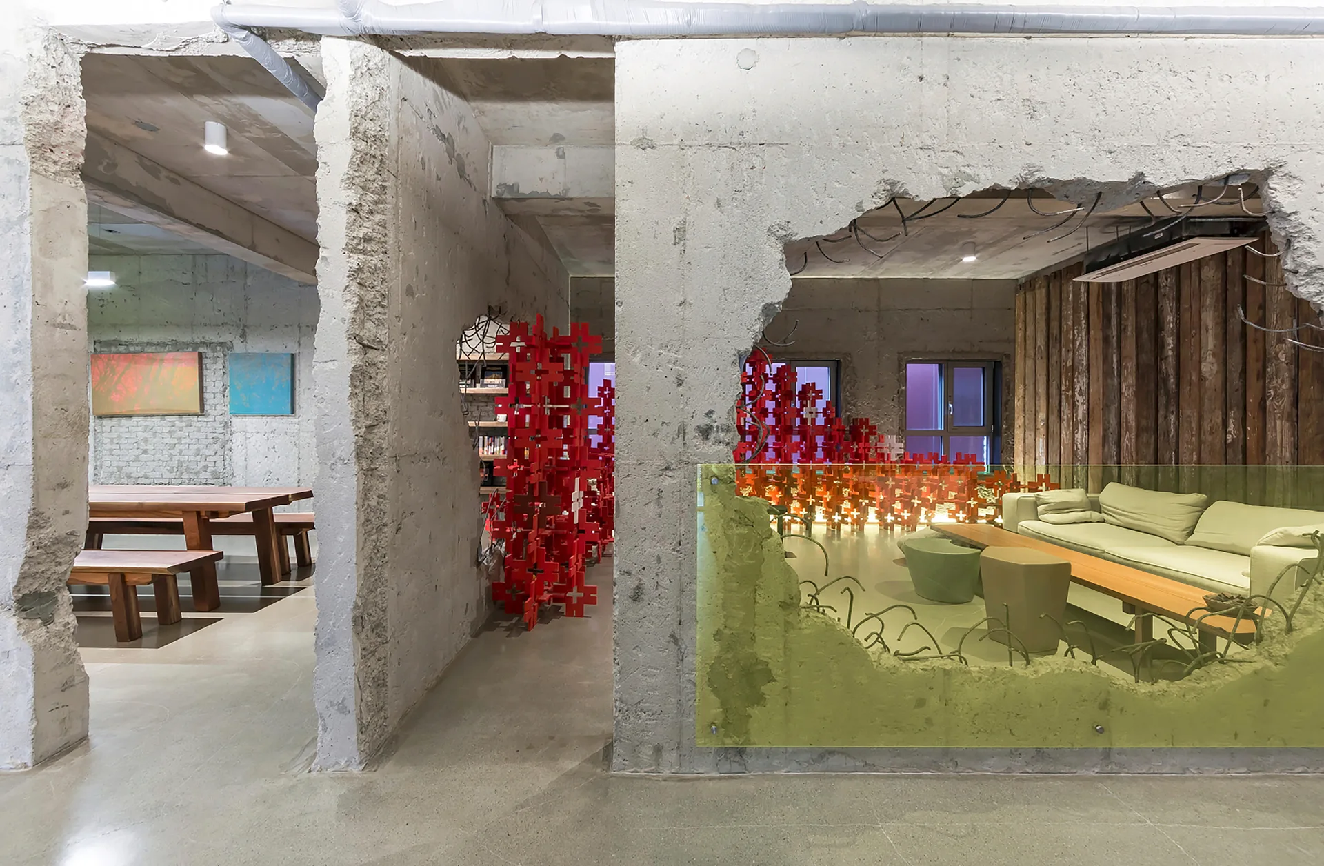 An industrial interior features raw concrete walls with jagged broken openings, a yellow glass panel, and a bright red modular partition screen.