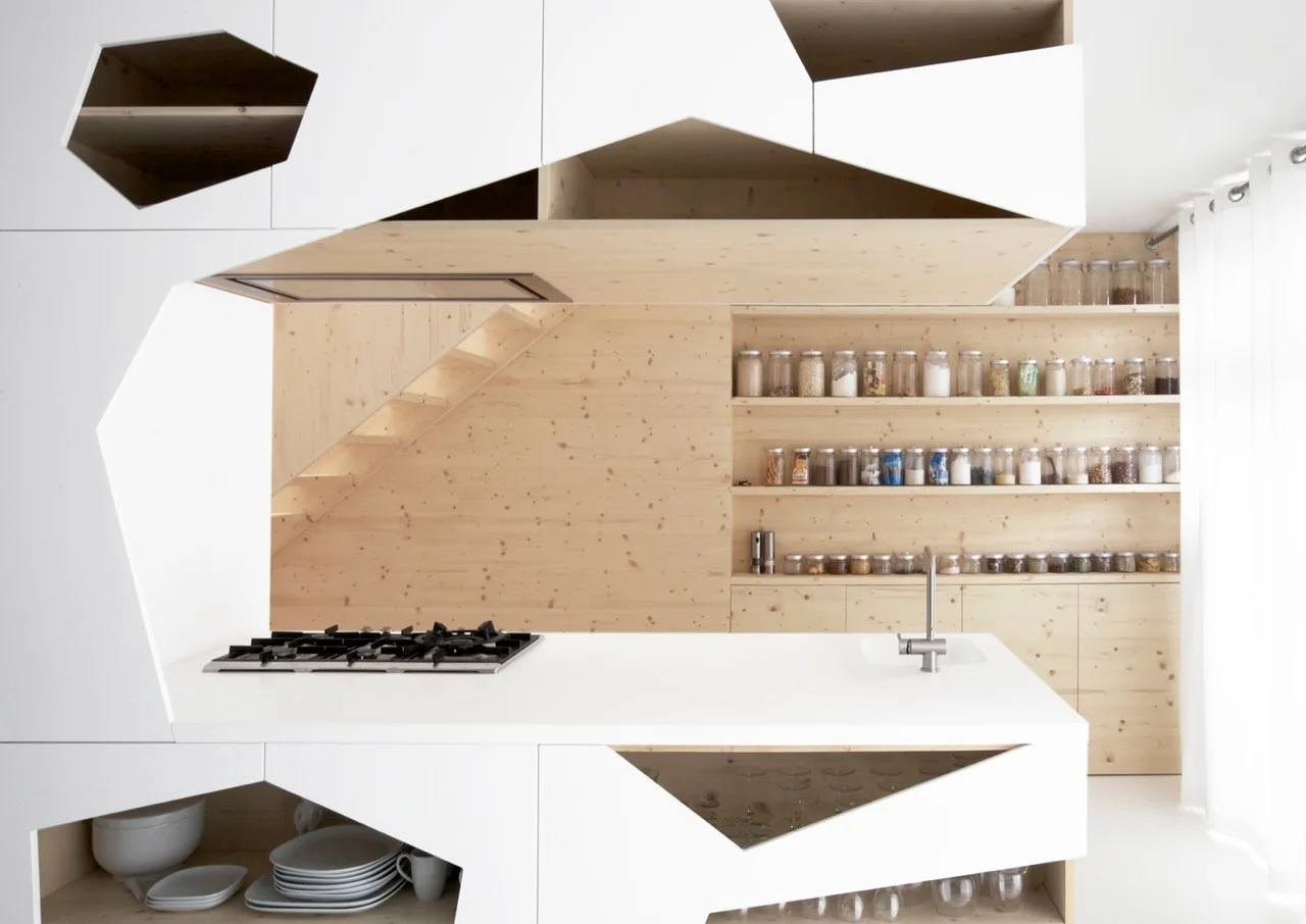 A modern kitchen featuring white cabinets with geometric cutouts, a gas cooktop, and light pine wall paneling with open pantry shelves.