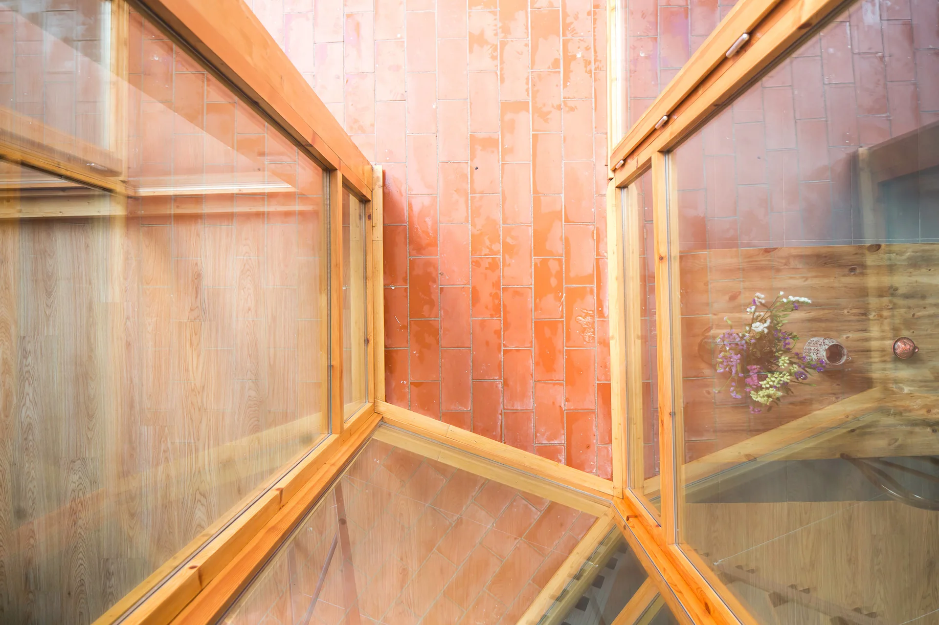 A high-angle view looking down into a courtyard featuring orange terracotta tile flooring and natural wood-framed glass enclosures.