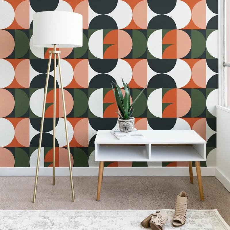 A white mid-century modern console table and brass tripod floor lamp stand in front of bold geometric patterned wallpaper in terracotta, green, and black.