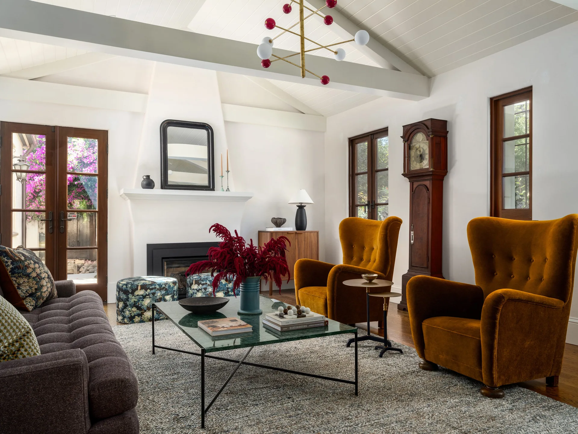 An eclectic living room features two mustard yellow velvet armchairs, a green marble coffee table, and a white fireplace beneath a vaulted ceiling.
