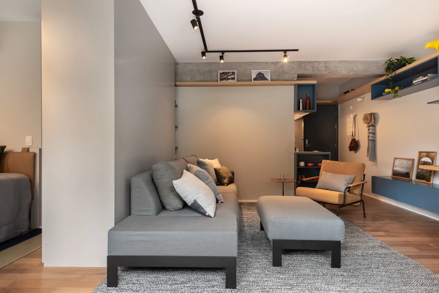 A contemporary living room featuring a grey sectional sofa, a yellow armchair, black track lighting, and blue floating wall shelves.
